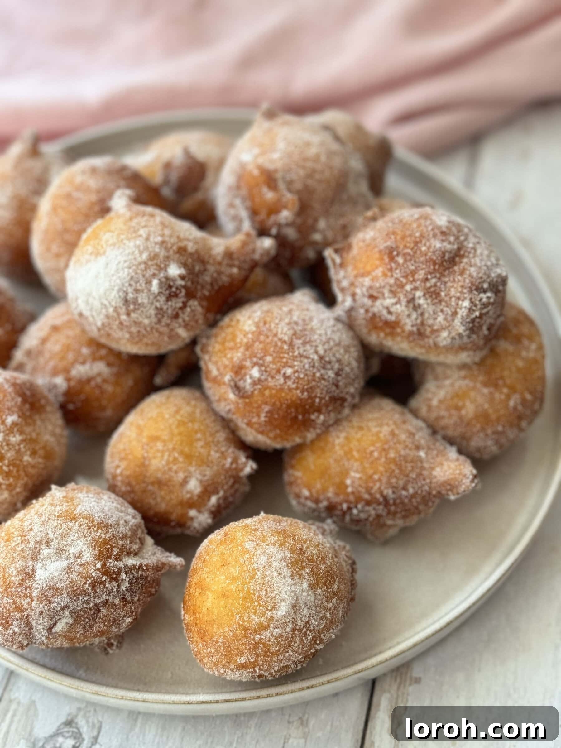 Pillowy Italian Sfingi Doughnuts 2 Golden brown Sfingi (Sicilian ricotta doughnuts) piled on a plate, lightly dusted with sugar, ready to be served.