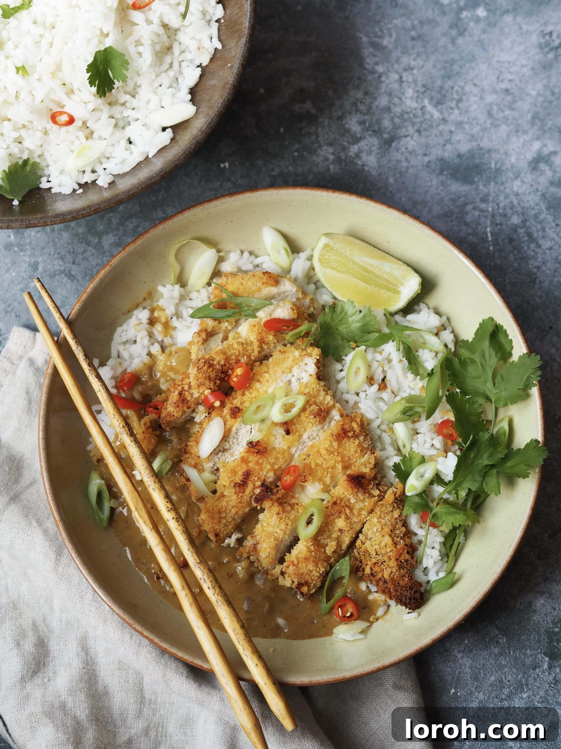 An inviting overhead view of a perfectly plated chicken katsu and curry sauce rice bowl, set against a stylish grey stone background, showcasing the vibrant colours and appealing textures of the dish.