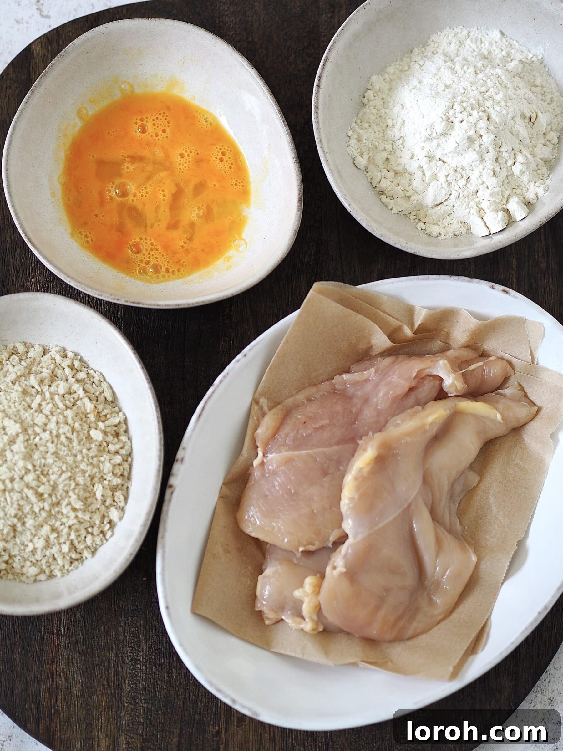 Three separate bowls arranged for the breading stations: one with plain flour, one with beaten egg, and one with golden panko breadcrumbs, ready for coating chicken cutlets.