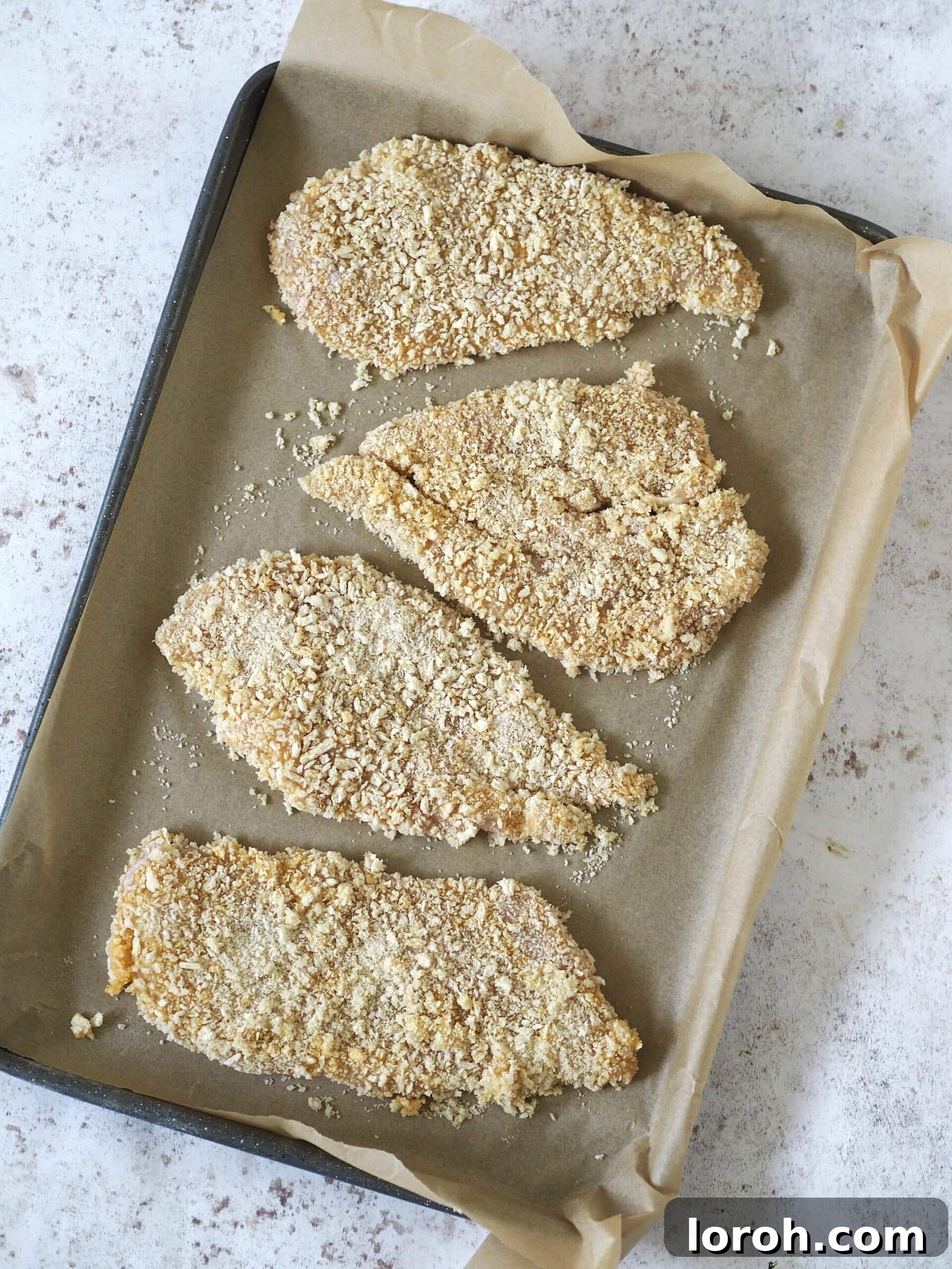 Two panko breadcrumb-coated chicken cutlets neatly arranged on a baking tray lined with parchment paper, ready for baking to golden perfection.
