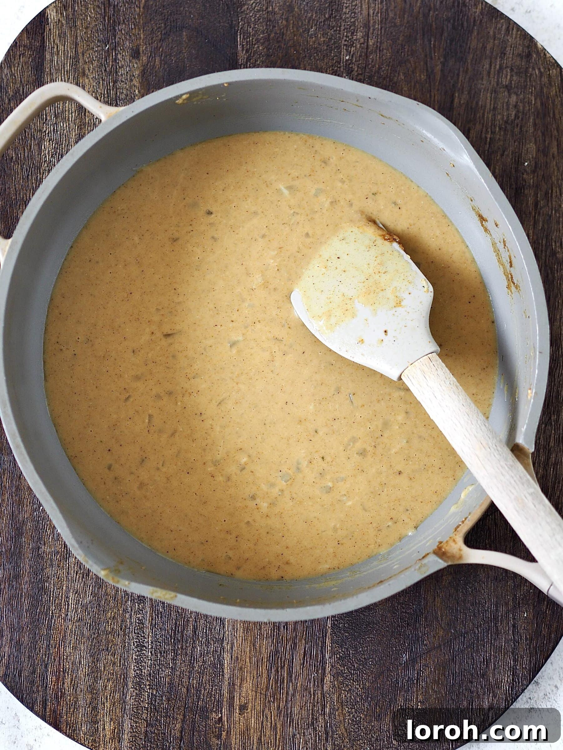 A rich and creamy Japanese curry sauce simmering gently in a grey frying pan, with visible pieces of onion, ginger, and spices, developing its complex flavors.