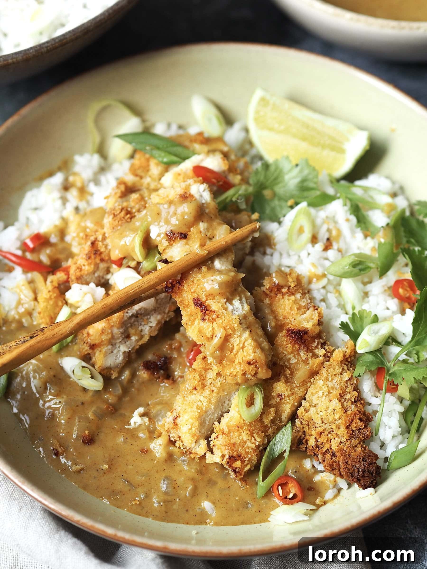 Elegant wooden chopsticks expertly picking up a succulent piece of crispy chicken katsu from a vibrant curry rice bowl, showcasing the golden crust and rich sauce.