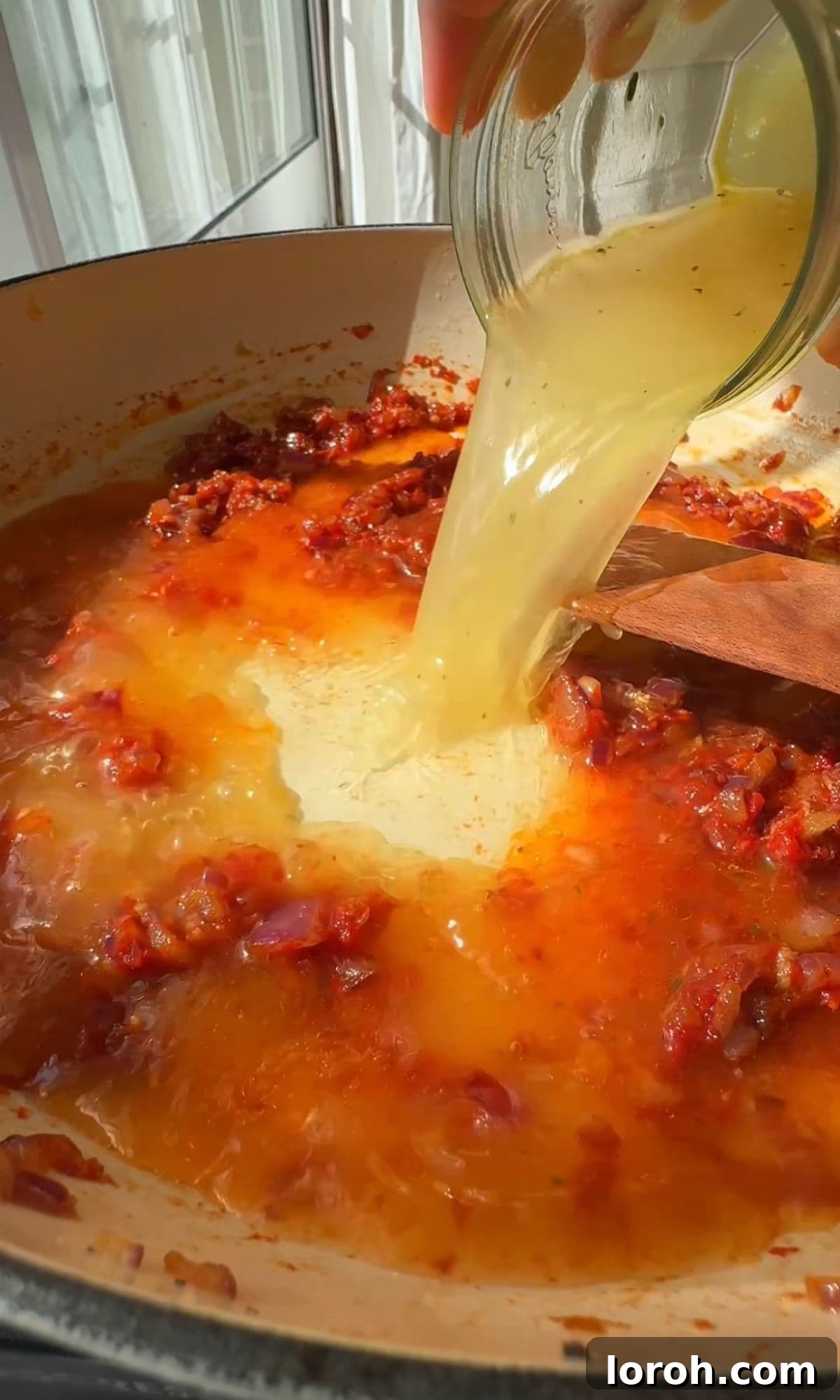 Pouring chicken stock into the sauce.