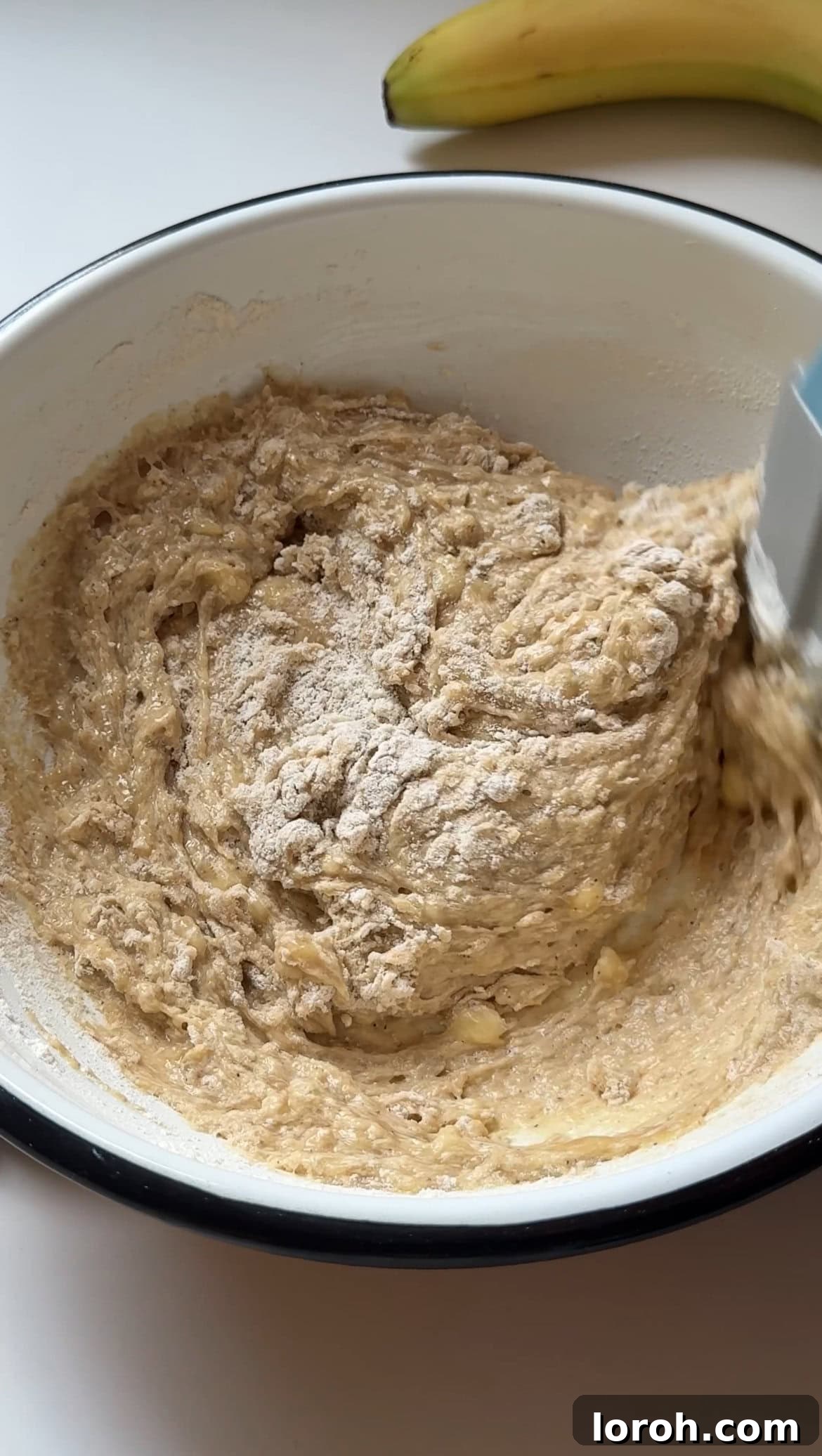 Gently folding flour into the wet muffin batter.