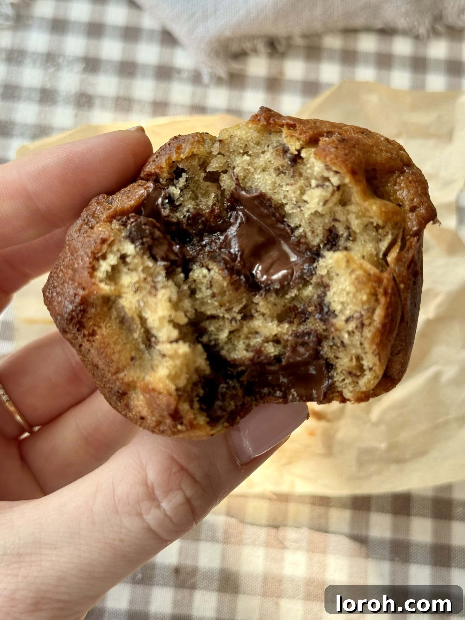 Woman holding a freshly baked banana chocolate chunk muffin, showing its rich, soft texture.