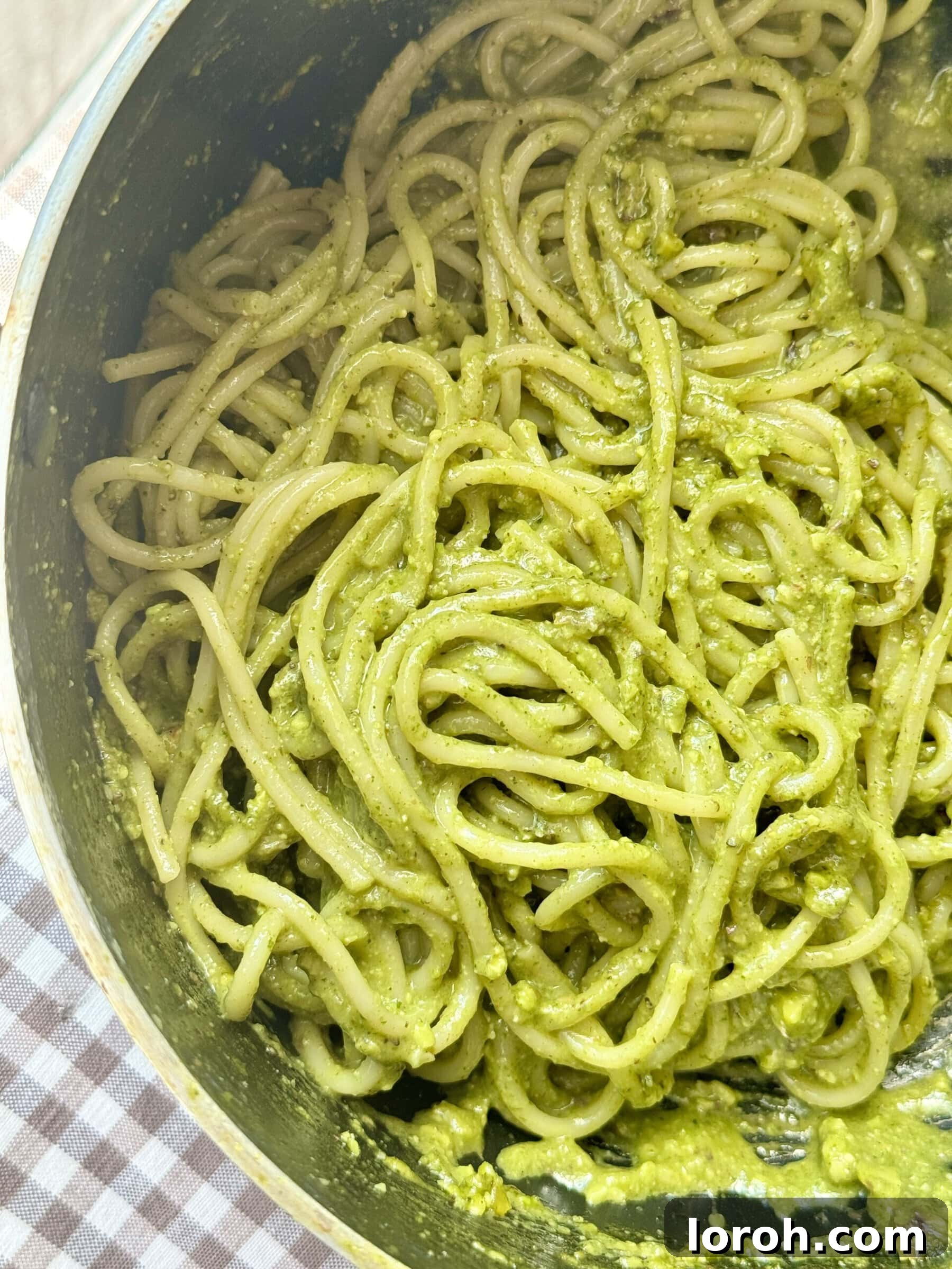 Close-up of spaghetti coated in vibrant green Pistachio Pesto, ready to be served.