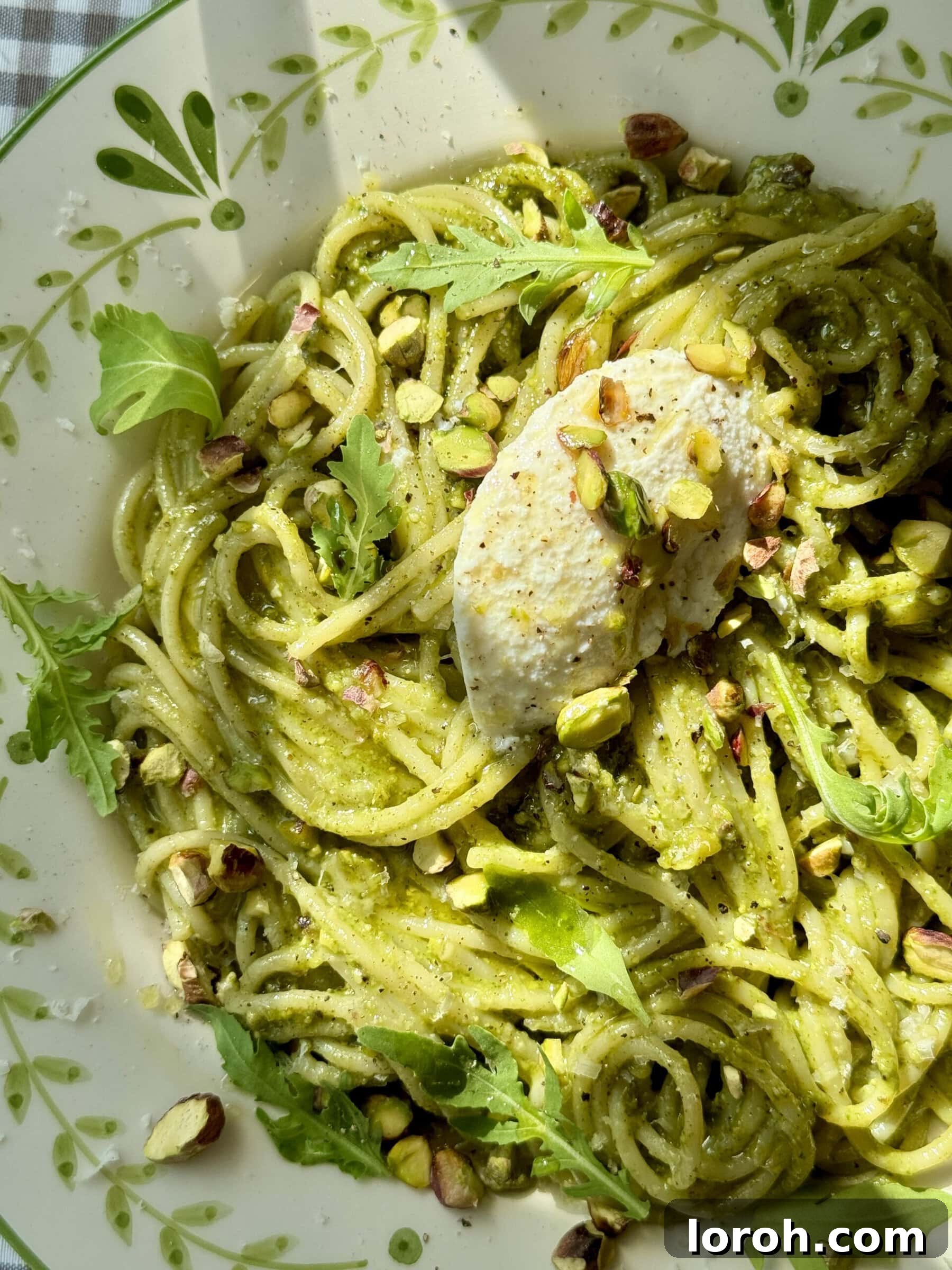 A serving of Pistachio Pesto Pasta, garnished with fresh basil leaves and a sprinkle of Parmesan.