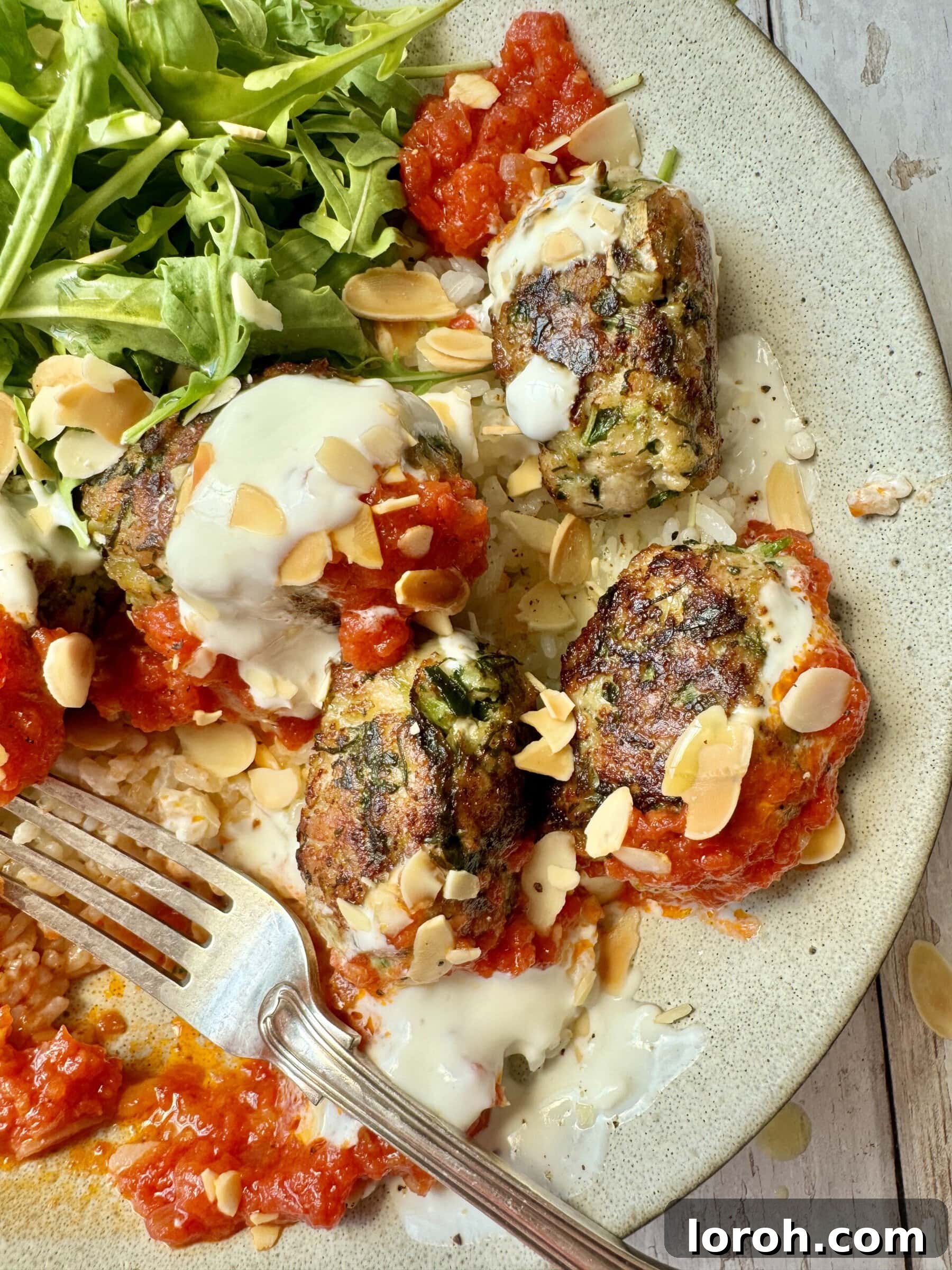Spicy Tomato Chicken Kofta Bowls 10 A hand reaching for a piece of chicken kofta from a bowl, highlighting its delicious appeal.