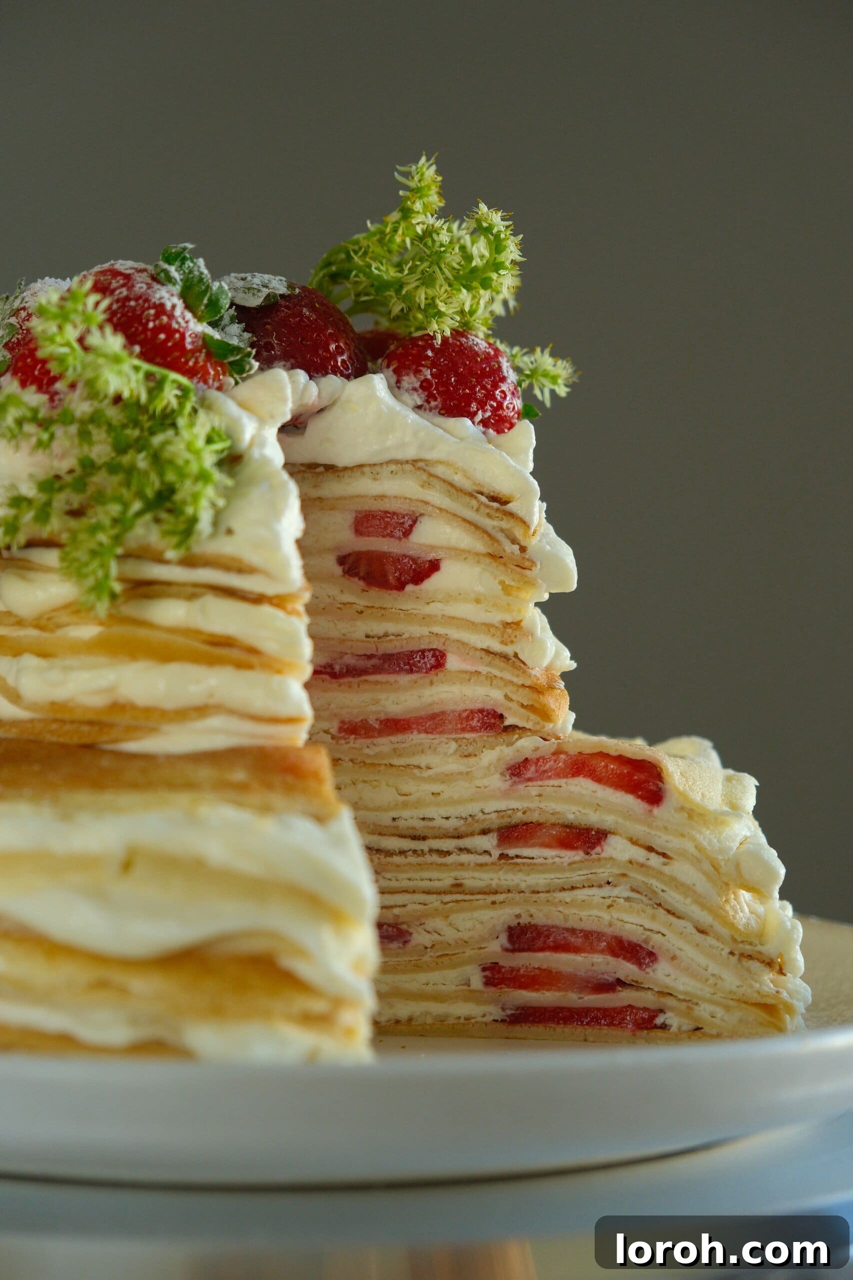 Cross-section of a delicious Strawberry Mille Crêpe Cake revealing delicate layers of crepe, white chocolate cream, and fresh strawberries.