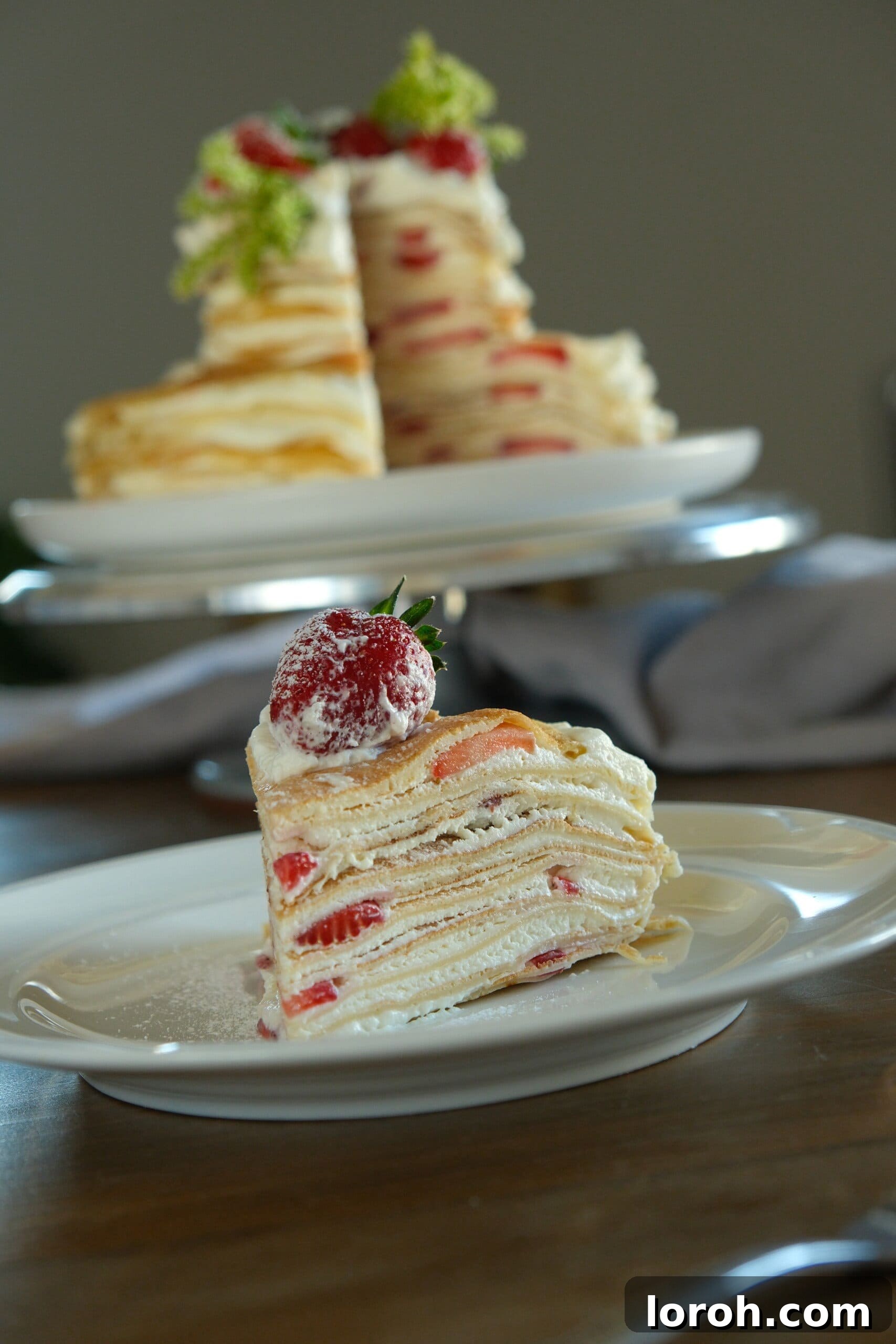 A perfectly sliced piece of Strawberry Mille Crêpe Cake, showing its many delicate layers on a white plate.