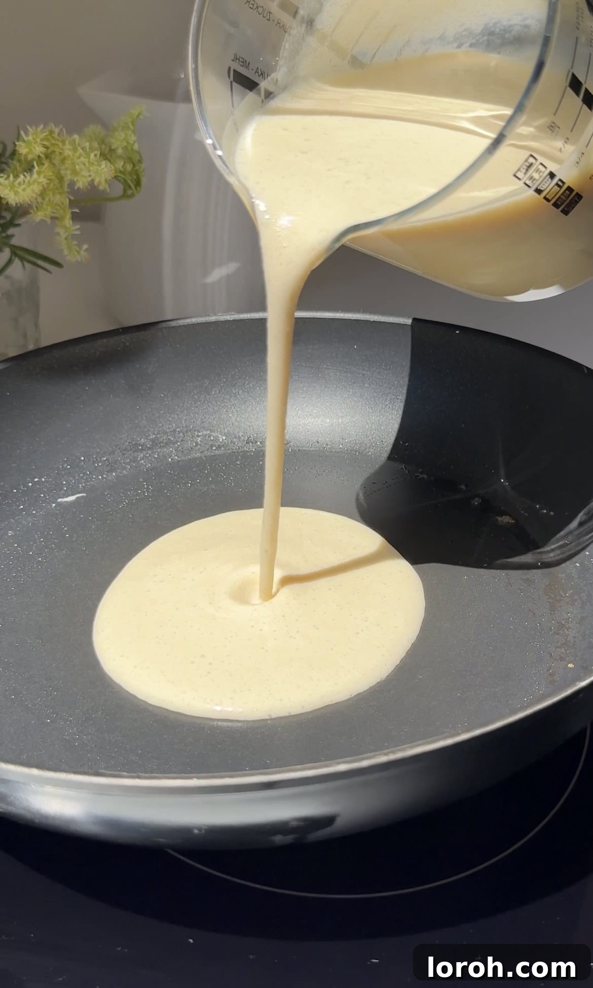 Pouring thin crepe batter into a hot non-stick pan to cook.