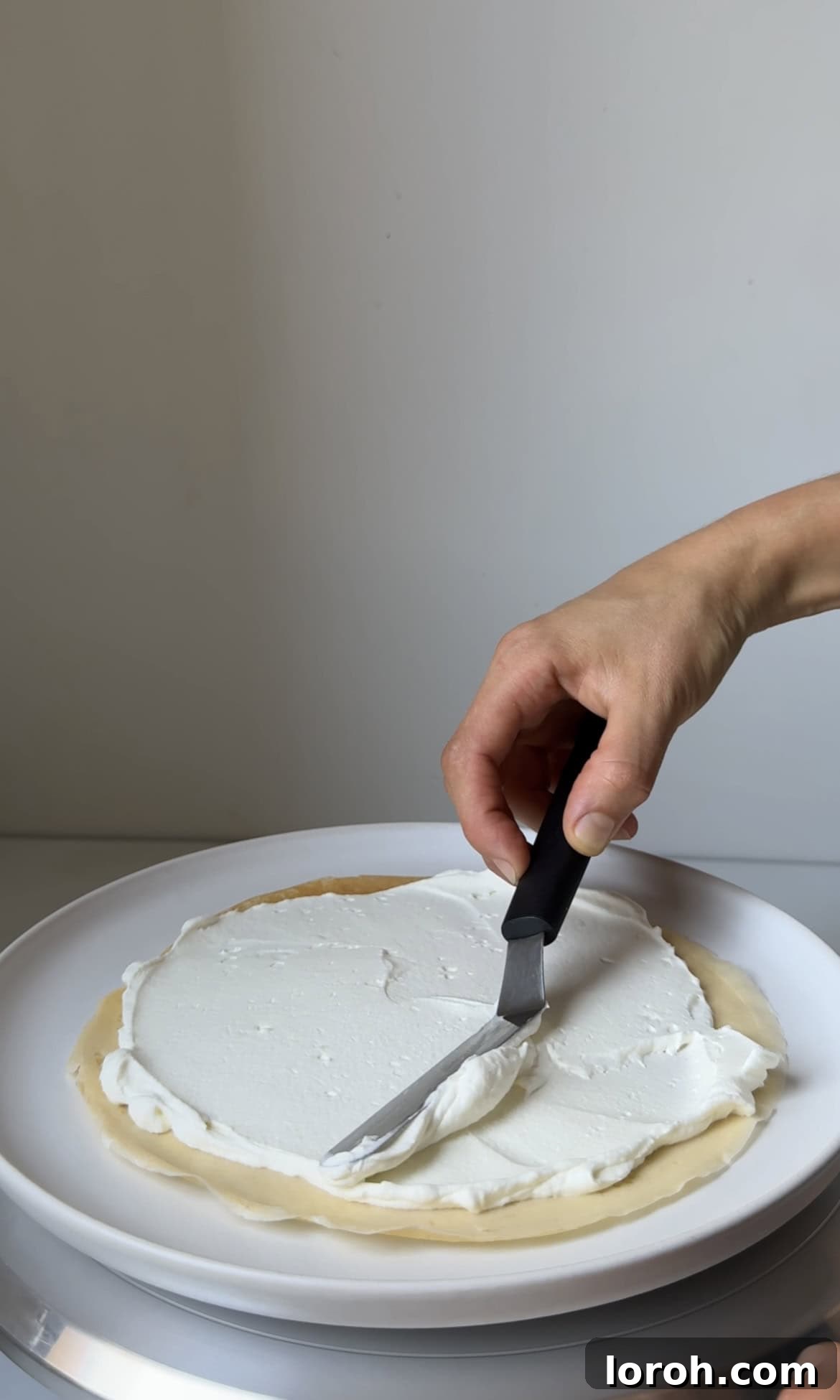 Spreading a thin, even layer of white chocolate cream onto a crêpe with a palette knife.