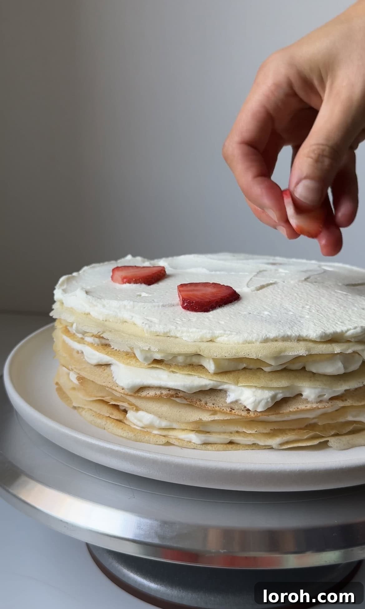 Adding a layer of fresh sliced strawberries over white chocolate cream on the mille crepe cake.