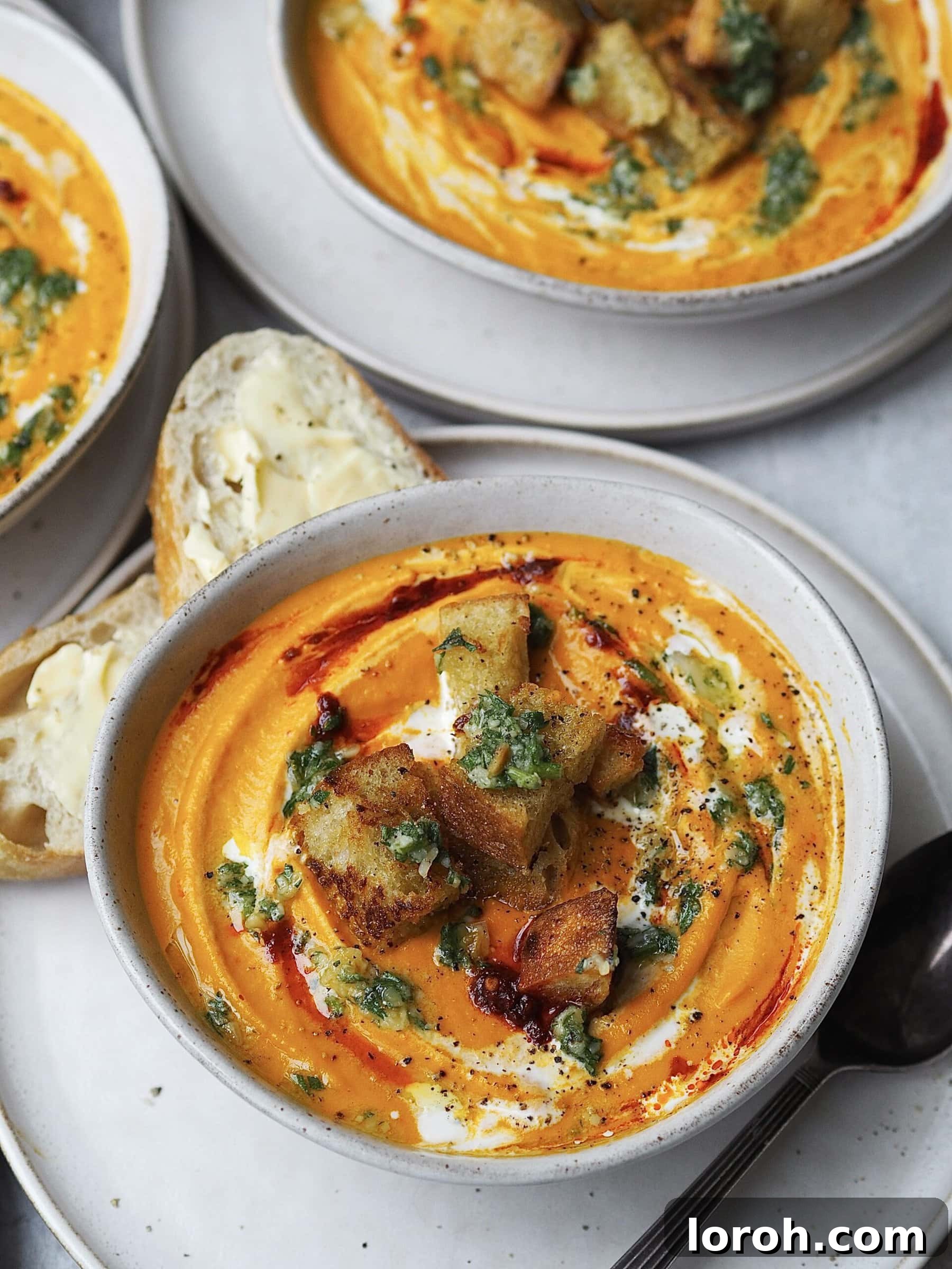 Smoky Harissa Carrot Velouté 2 Bowl of carrot soup swirled with cream, harissa, and topped with pesto and croutons.