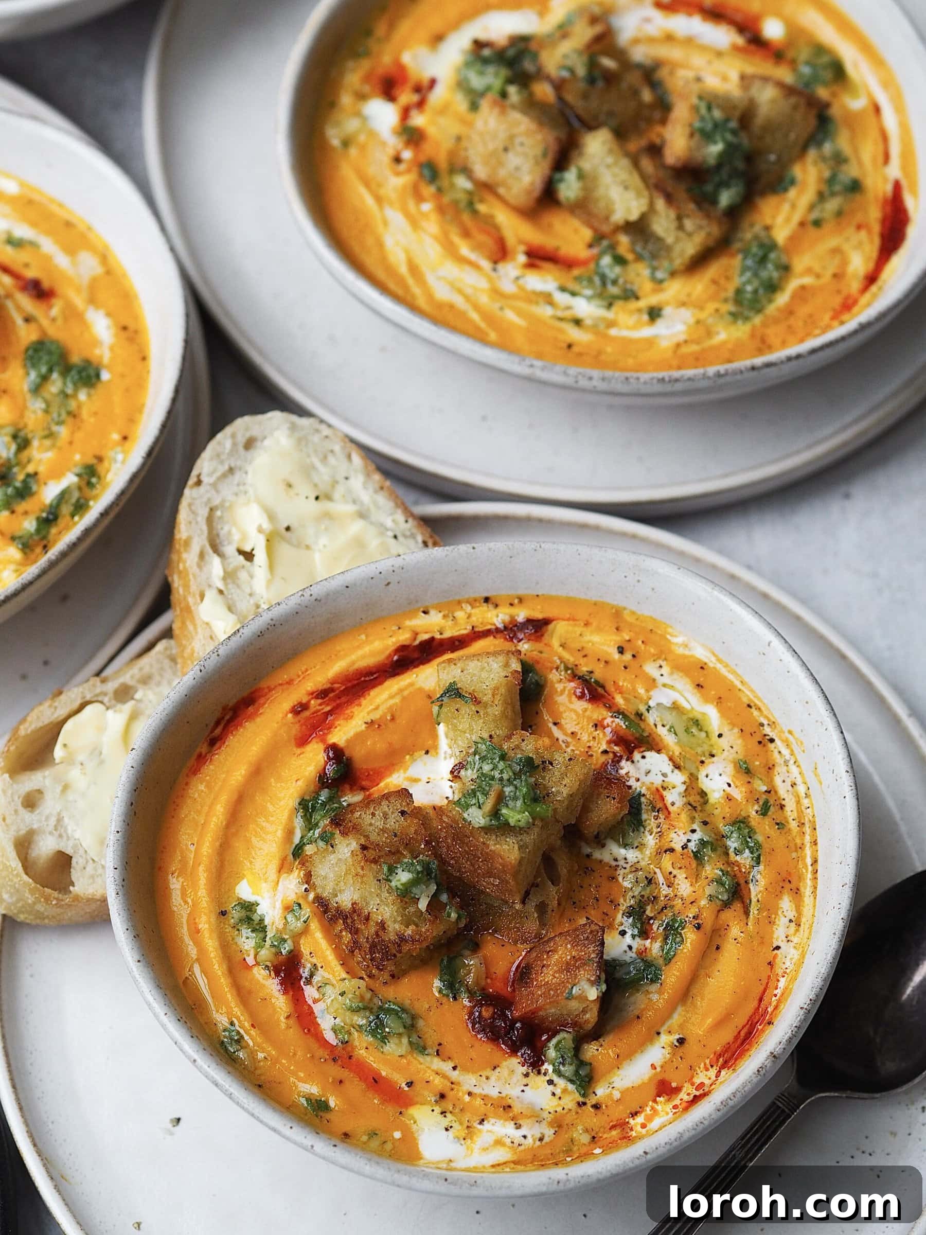 Smoky Harissa Carrot Velouté 11 Close up of a bowl of roasted carrot soup topped with cream, harissa, croutons and pesto.