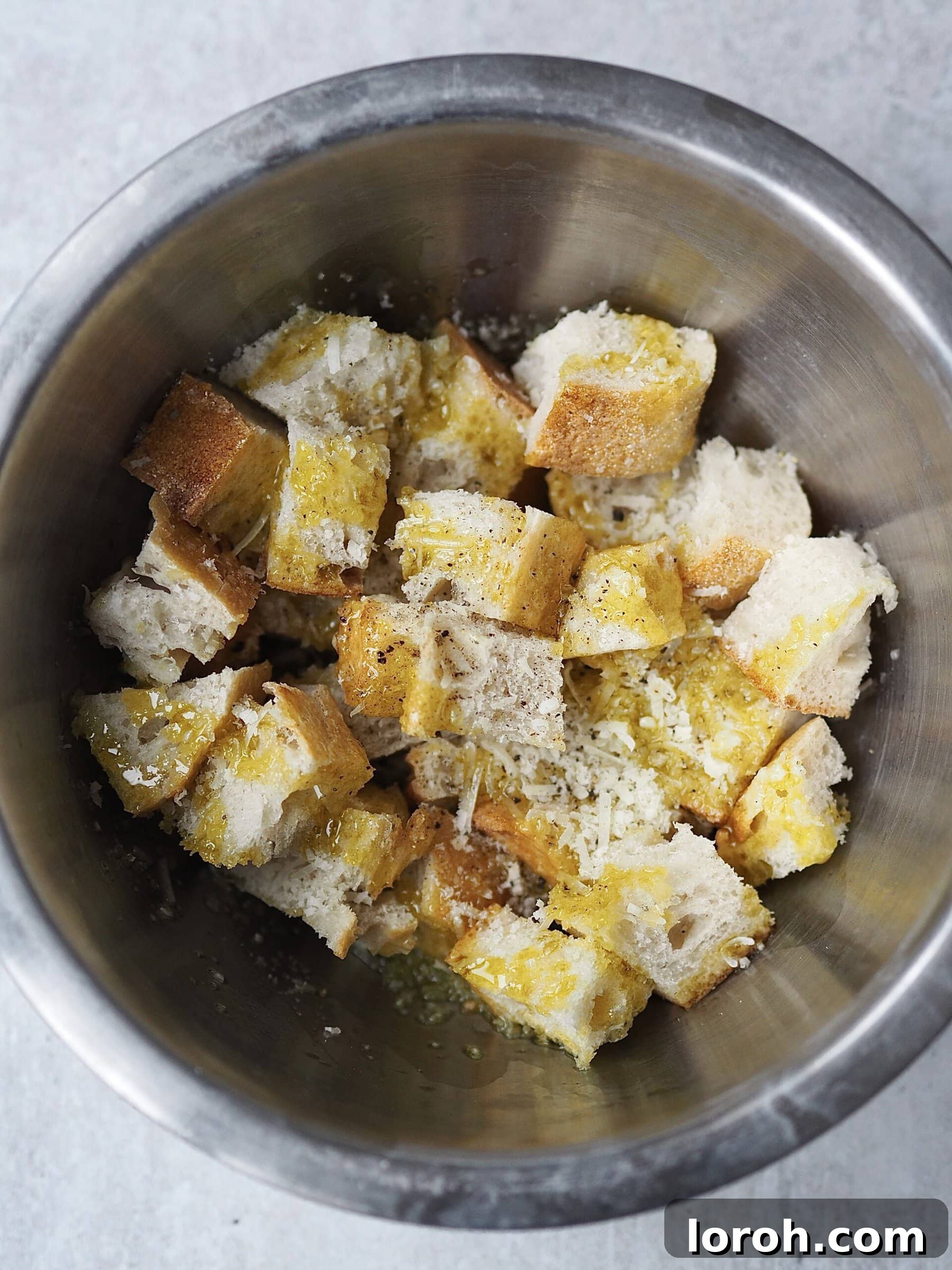 Smoky Harissa Carrot Velouté 8 Bread cubes tossed with grated cheese, olive oil and seasonings in a metal bowl.