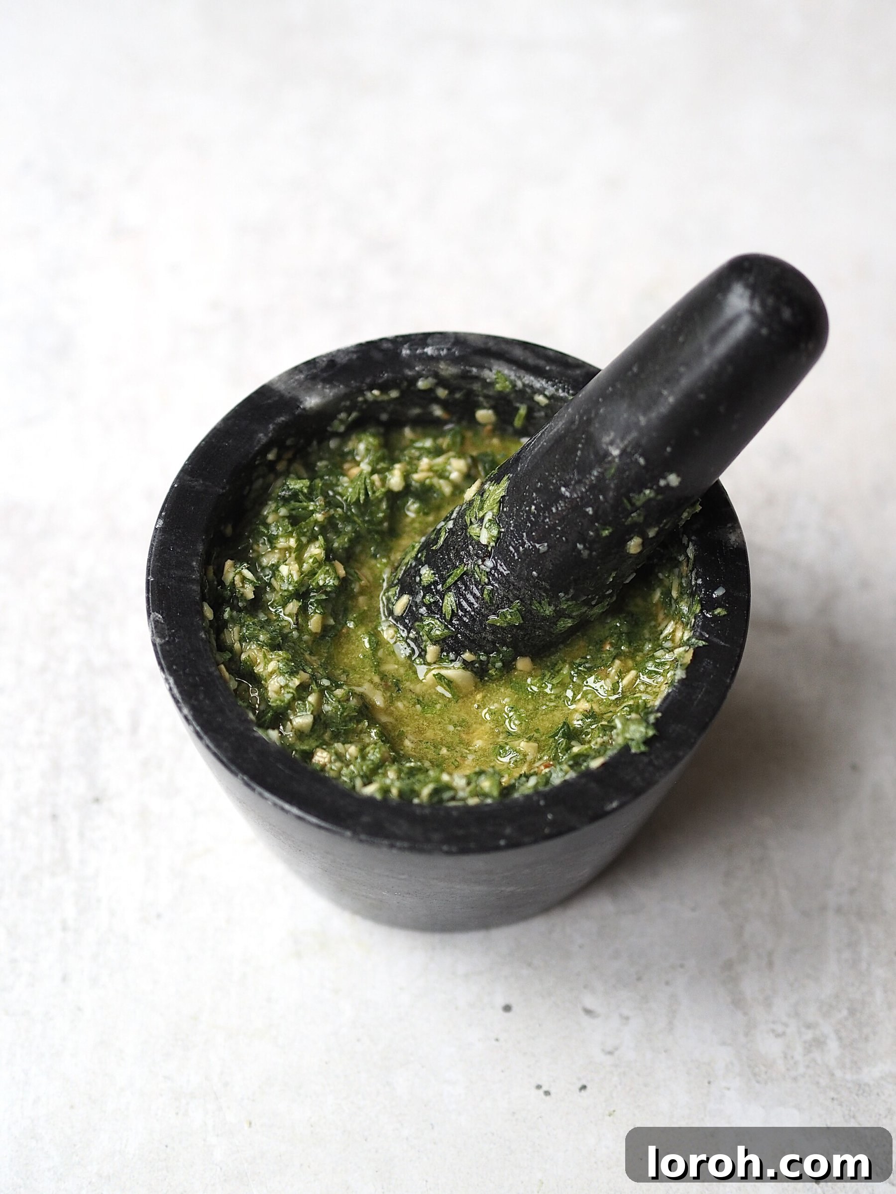 Smoky Harissa Carrot Velouté 10 Carrot top pesto being made in a dark grey mortar and pestle.