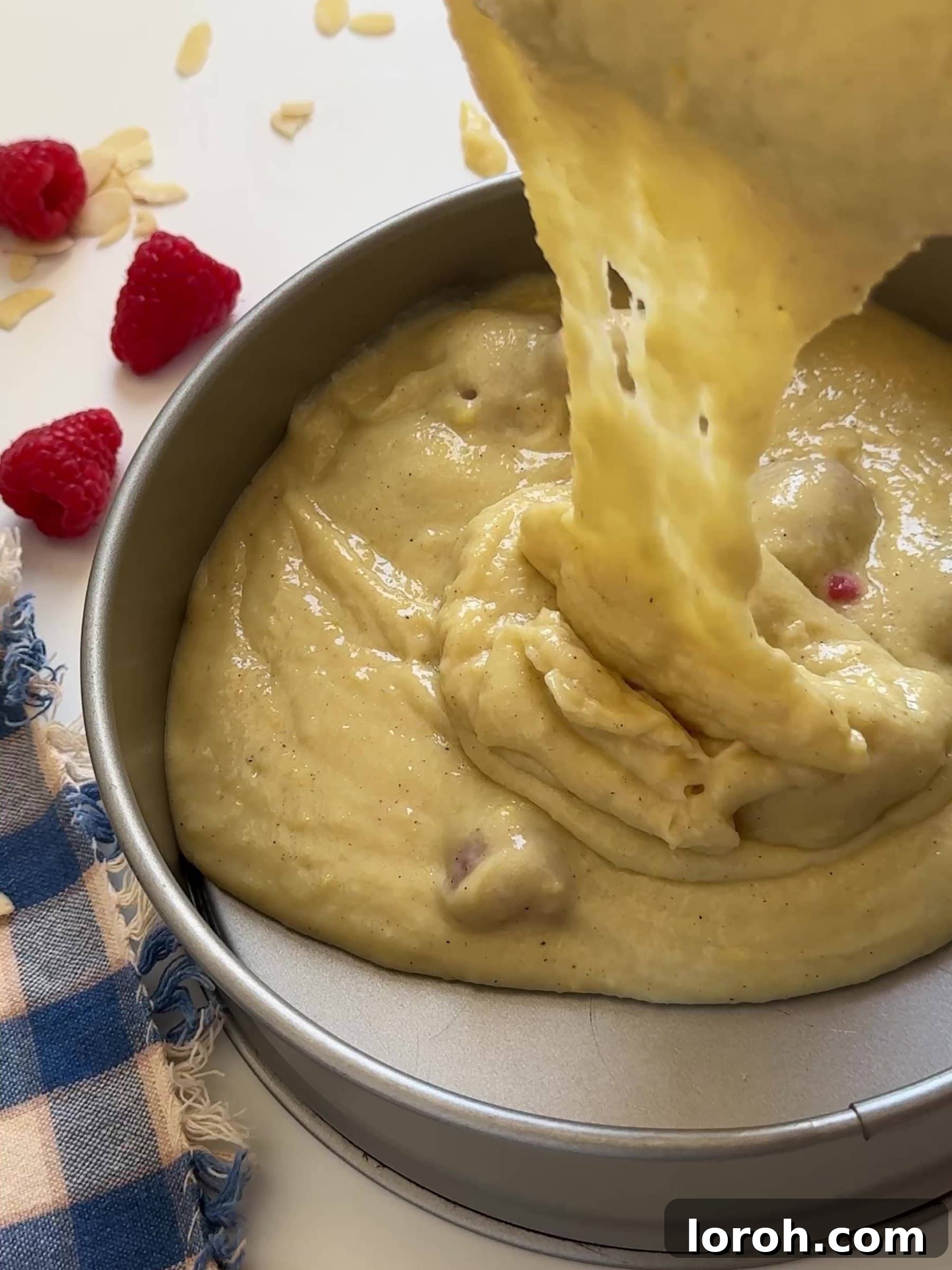 Divine Raspberry Almond Ricotta Cake 9 Pouring cake batter into a prepared springform tin, topped with remaining raspberries and flaked almonds.