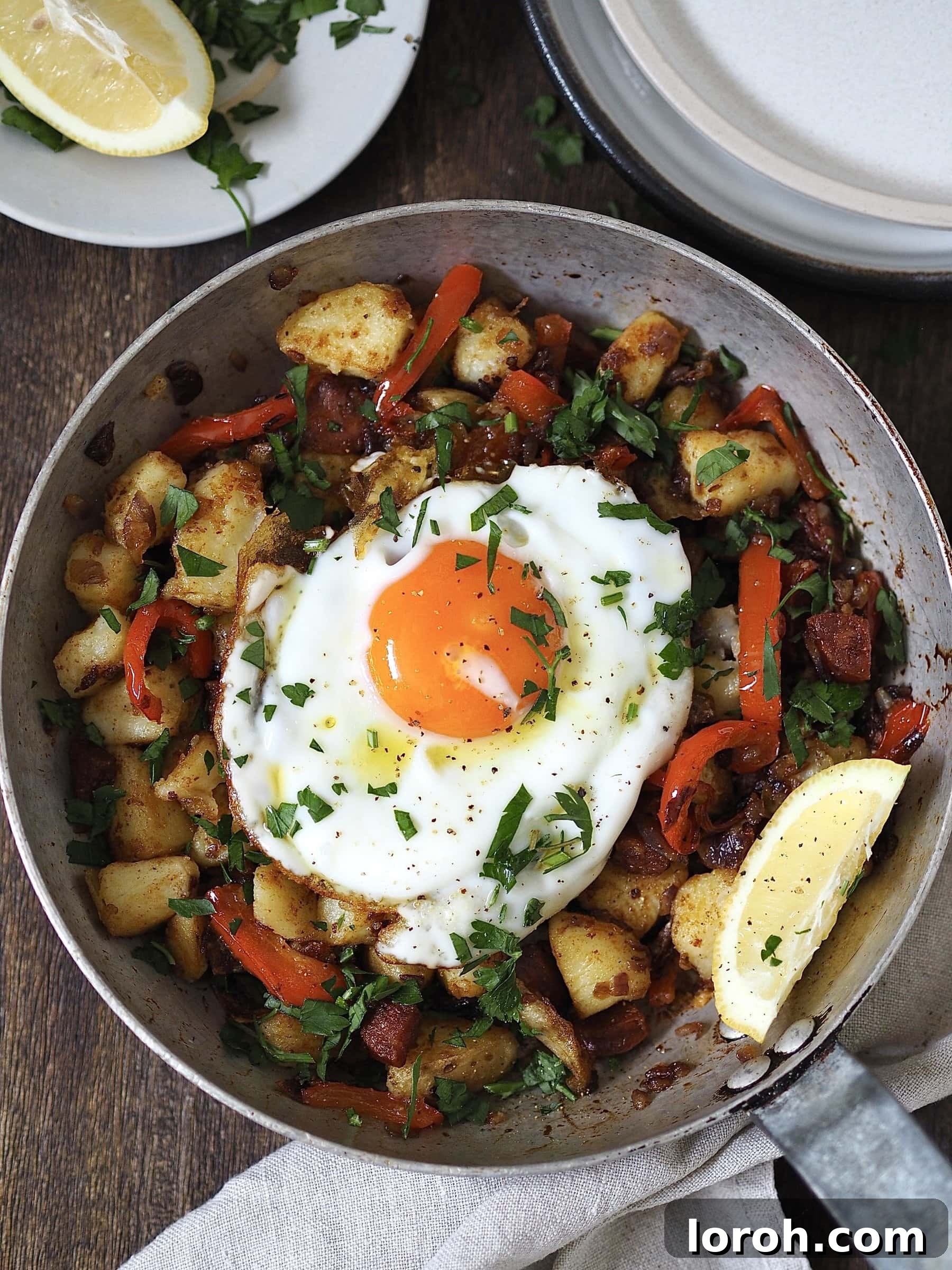 Spicy Chorizo and Golden Potato Morning Skillet 10 Serving Chorizo and Potato Breakfast Hash topped with a fried egg, fresh parsley, and lemon wedges on a plate.
