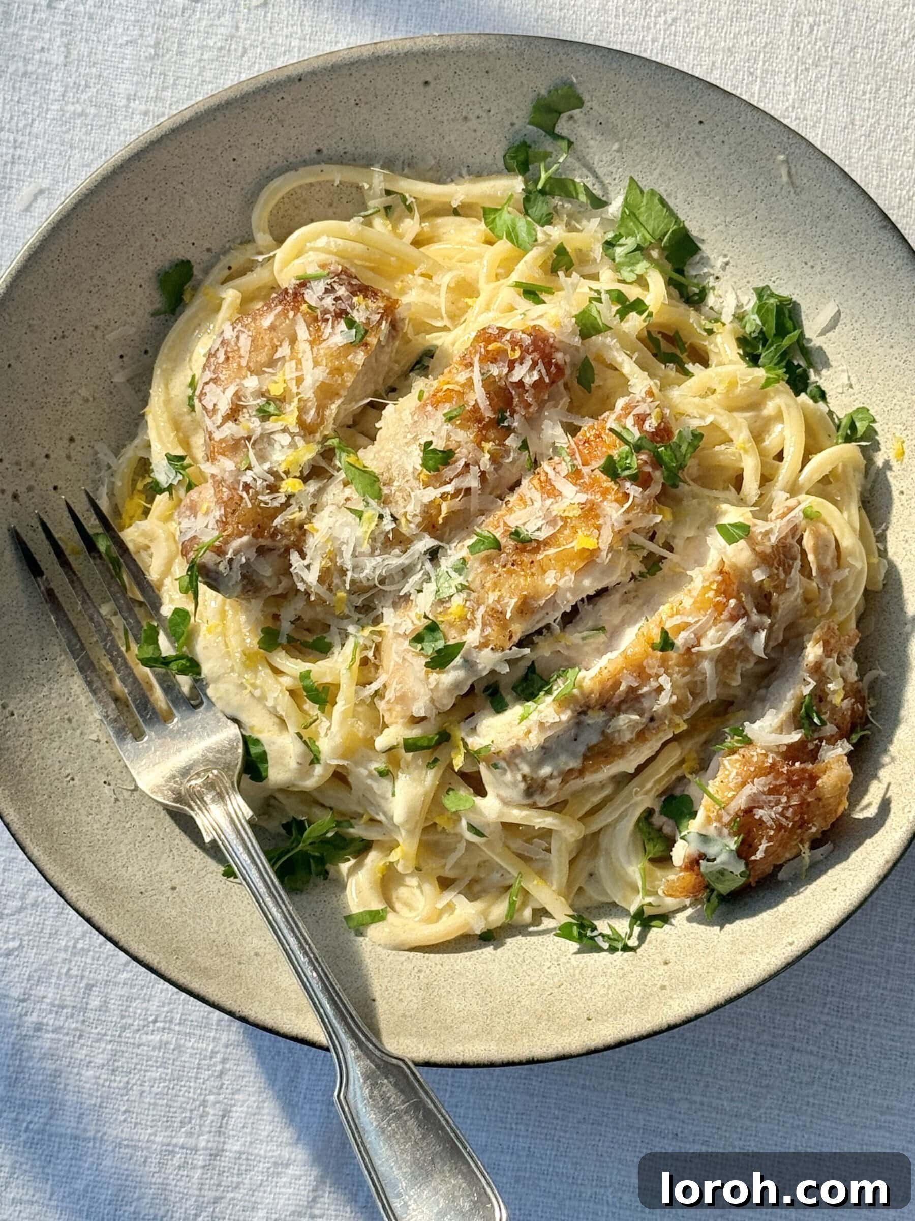 Velvety Chicken Pasta 3 A close-up of creamy chicken pasta served in a bowl, garnished with fresh parsley and lemon zest, with a fork ready to twirl.