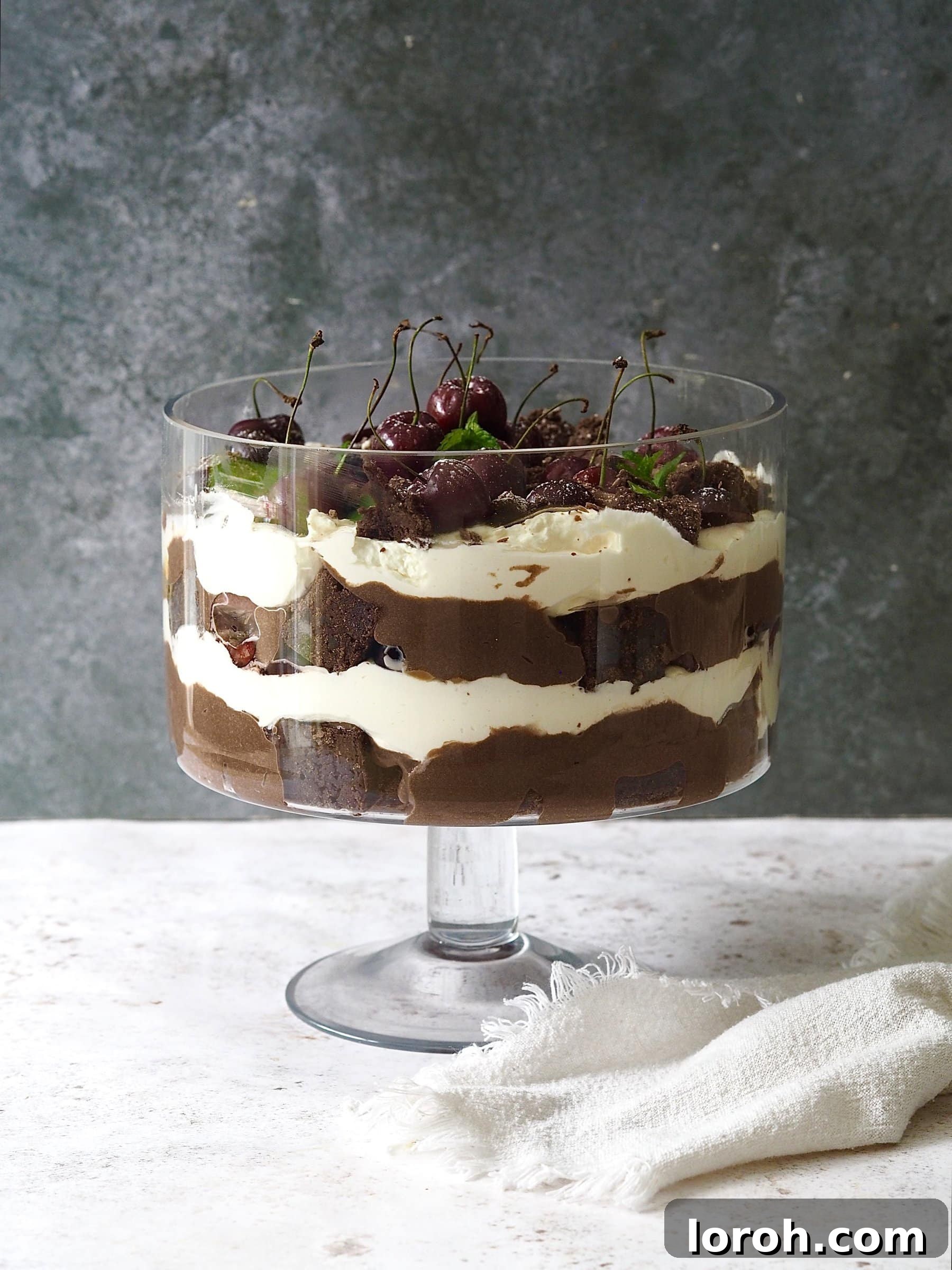 Stunning Chocolate Brownie Trifle in a glass bowl, layered with brownies, mousse, cream, caramel, and cherries, decorated for a festive occasion.