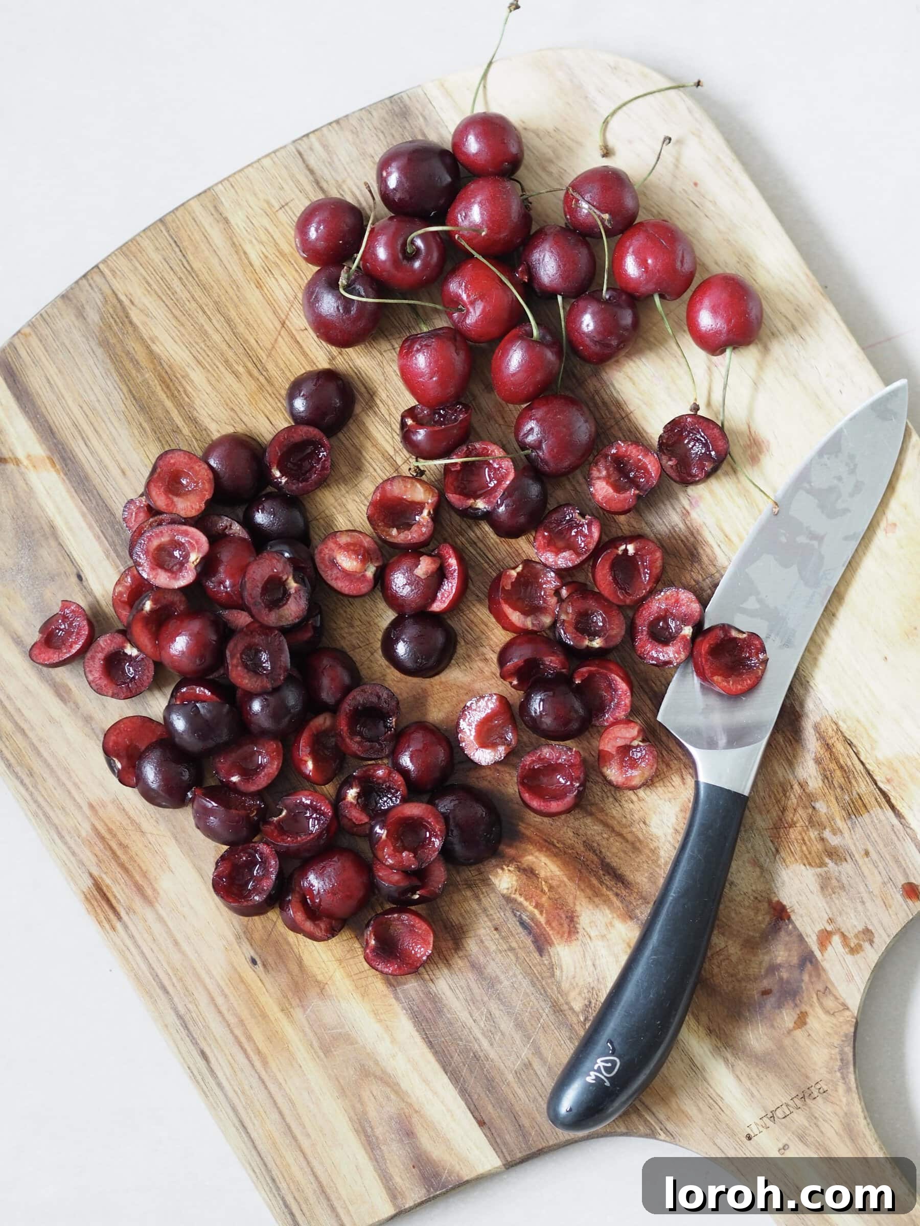 Close-up of fresh red cherries being cut and pitted on a cutting board, preparing them for the trifle.