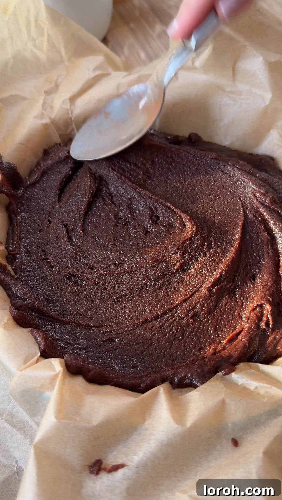 Spreading the rich brownie batter evenly into a parchment-lined baking tin before baking.