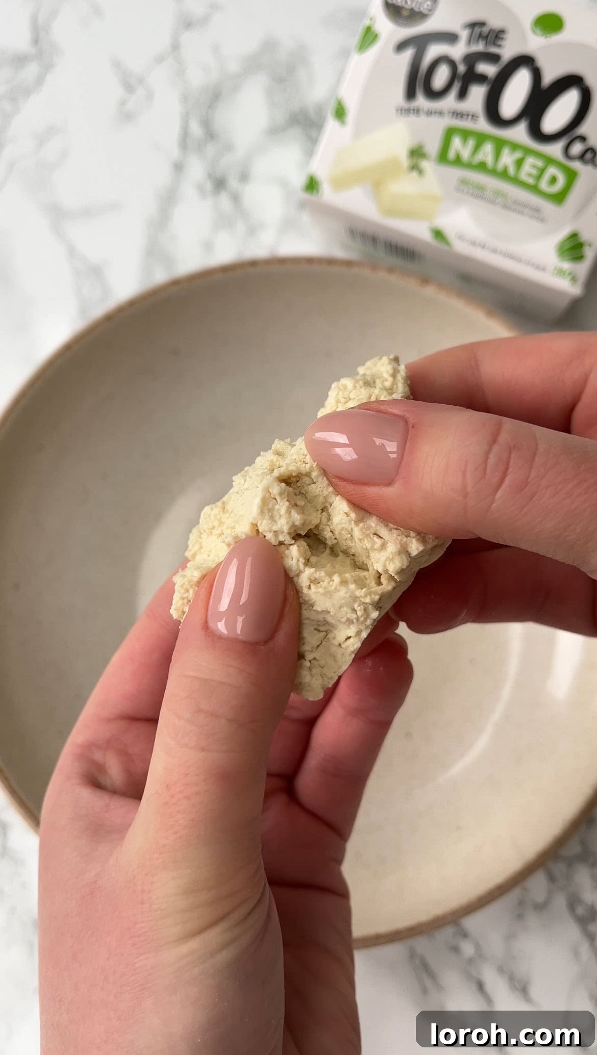 Tearing extra firm tofu into small chunks by hand, showcasing a rustic texture.