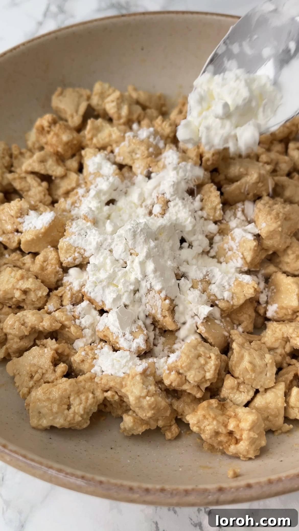 Savory Tofu Noodle Delight 6 Tofu chunks being sprinkled with cornstarch in a bowl, ensuring an even coating for maximum crispiness during frying.