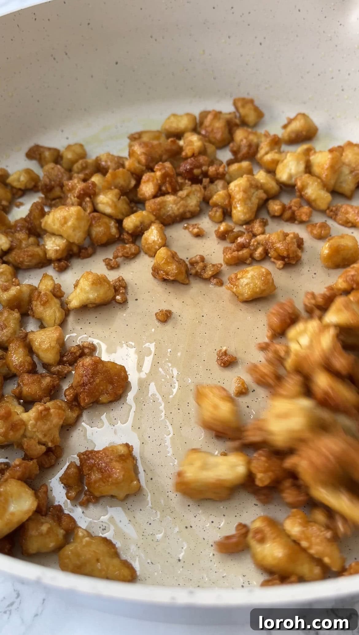 Frying cornstarch-coated tofu pieces in a non-stick pan until golden brown and crispy.