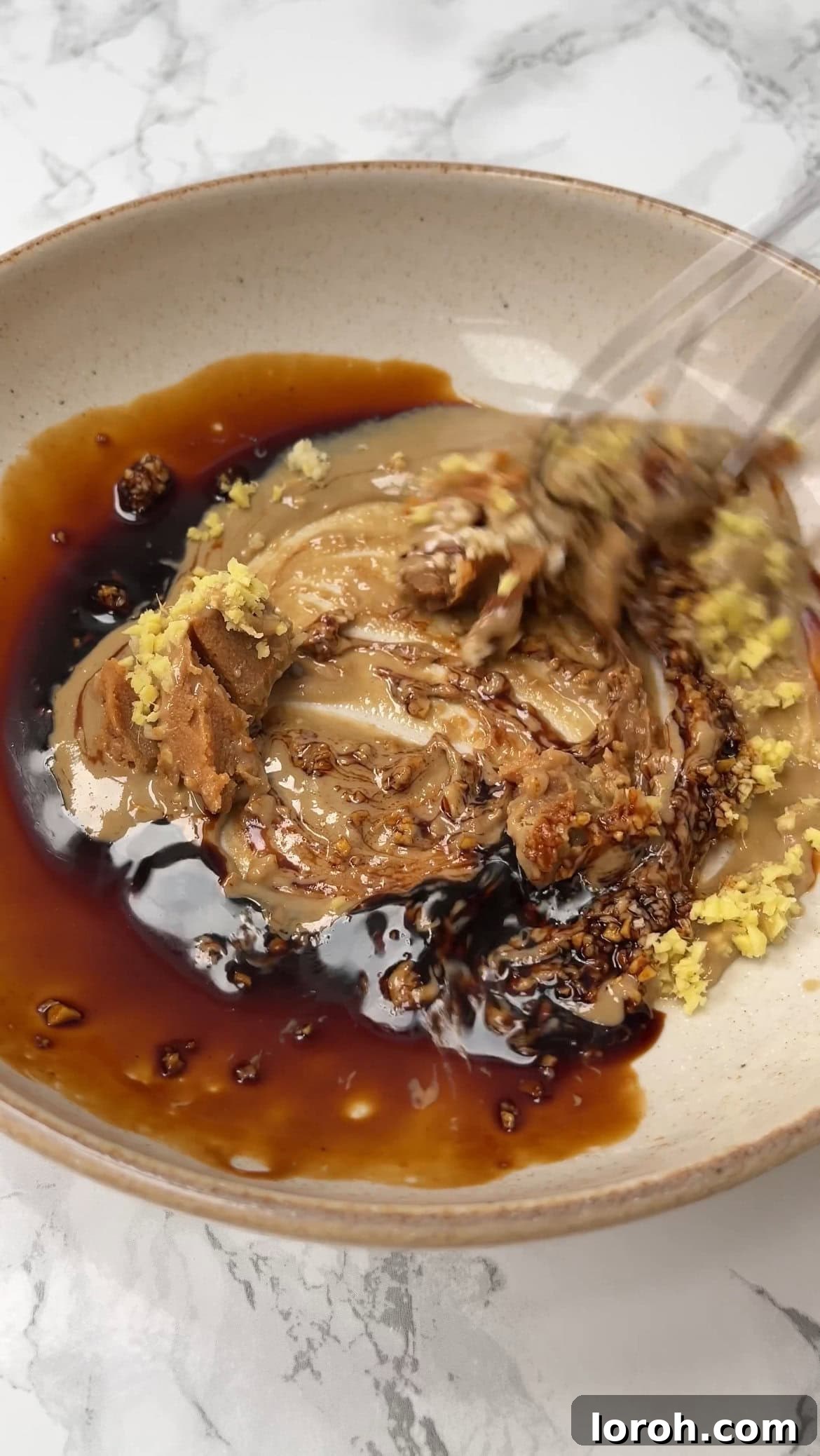 Whisking together miso paste, soy sauce, tahini, ginger, and garlic to form the soup base.