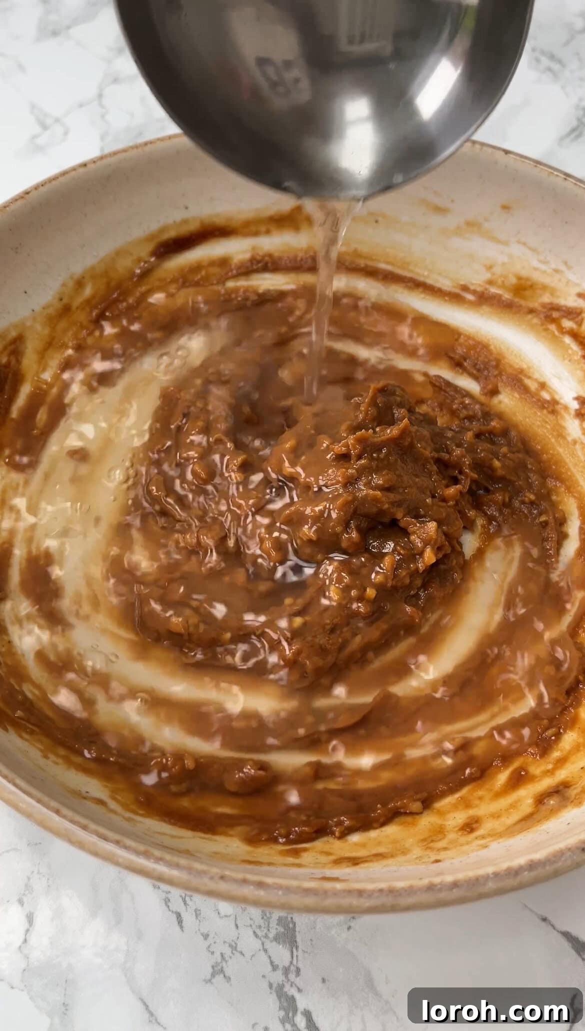 Adding a ladle of dashi stock to the whisked miso paste and other flavorings.