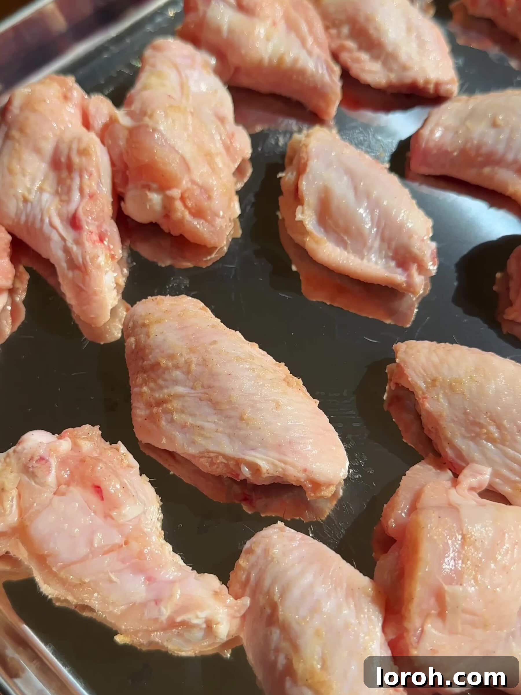 Arranging chicken wings on a baking tray with ample space for even cooking.