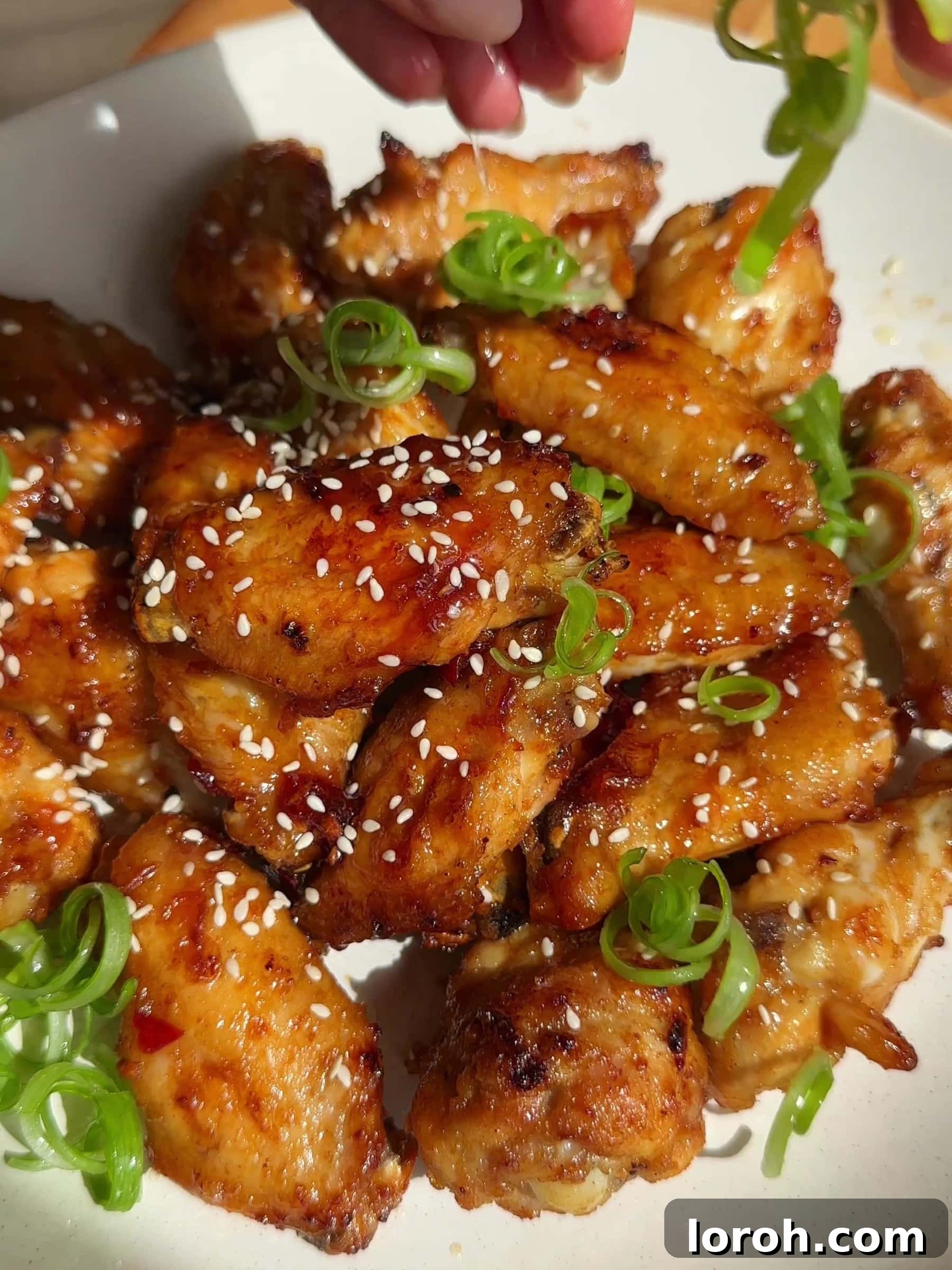 Garnishing Hot Honey Chicken Wings with sesame seeds and spring onions.
