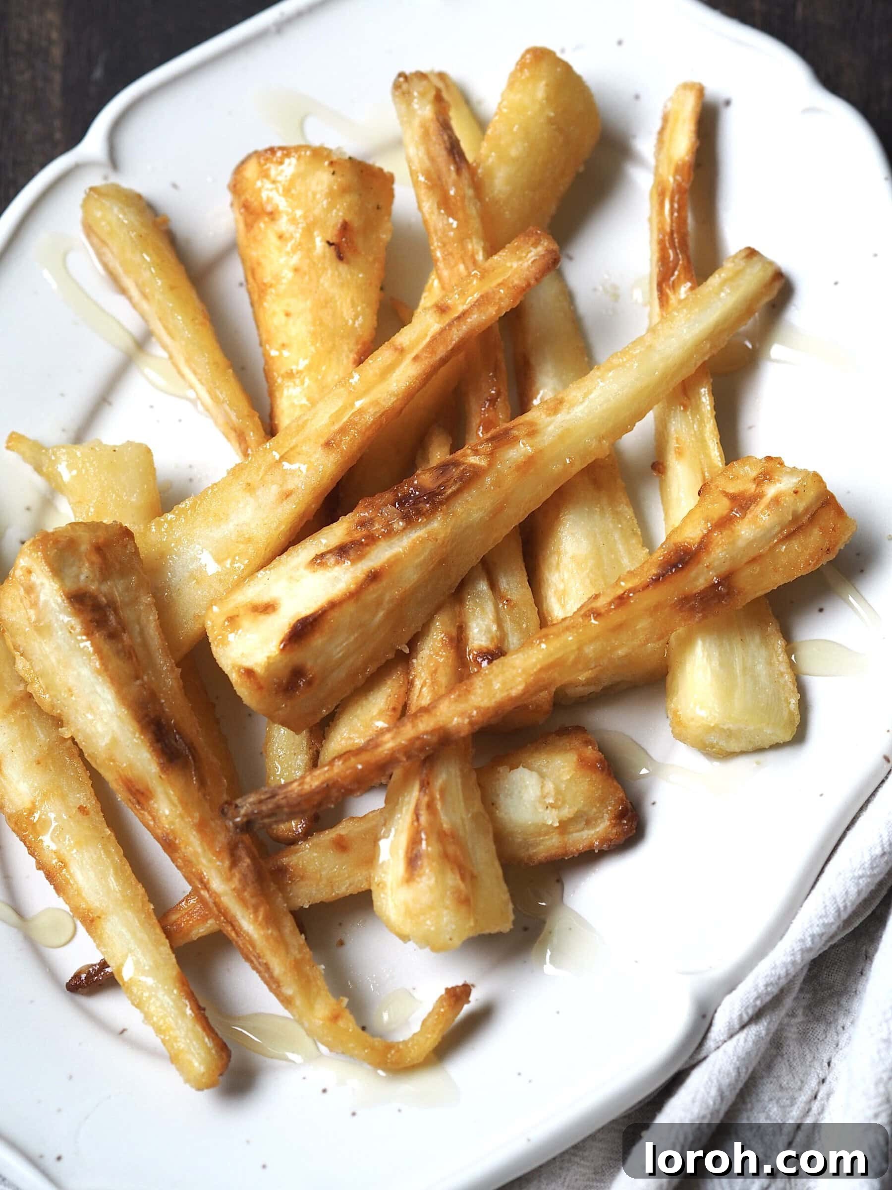 Close-up of golden honey glazed parsnips on a white serving platter, ready to be enjoyed.