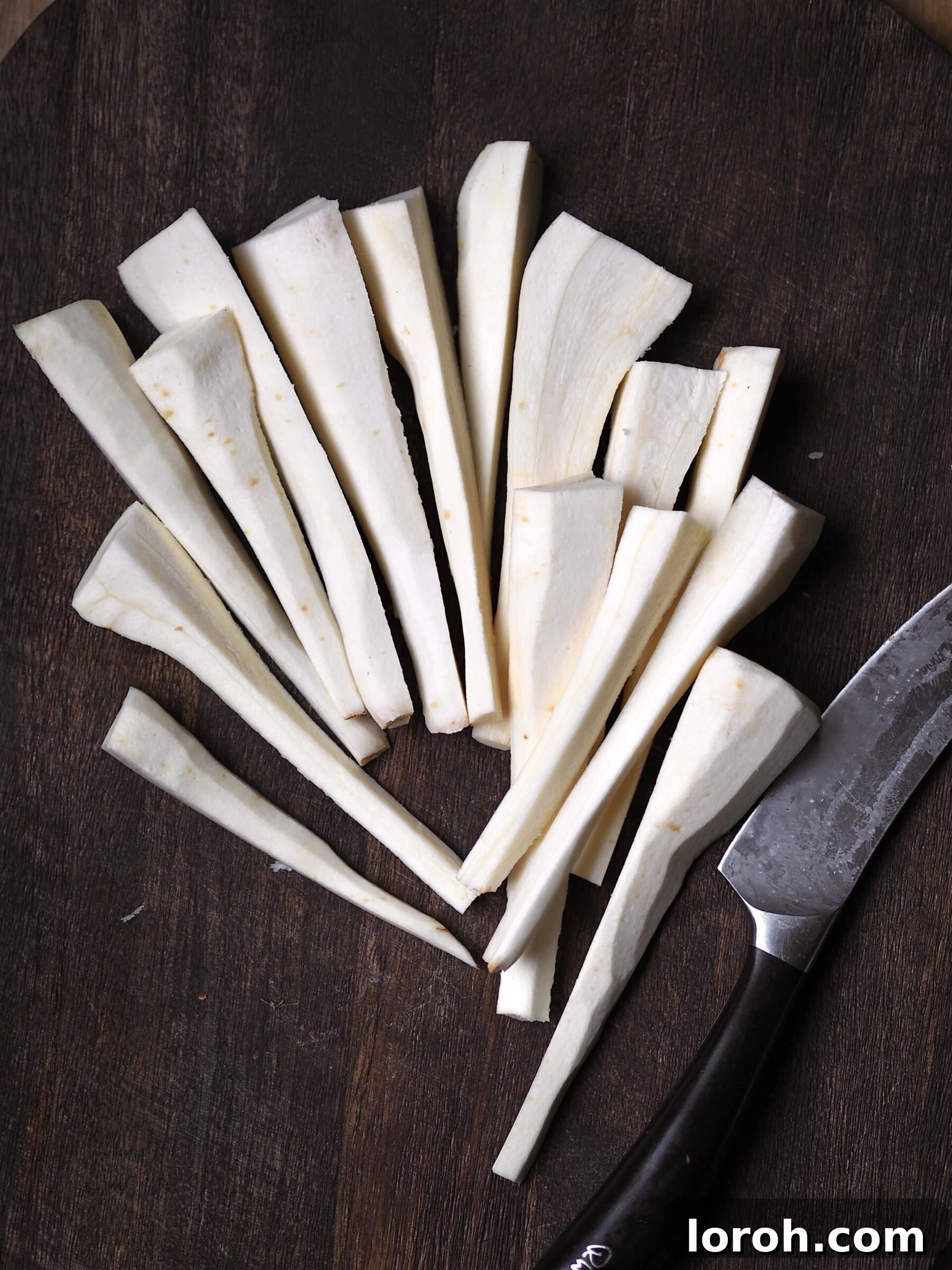 Fresh parsnips being sliced lengthwise on a wooden cutting board with a sharp knife.