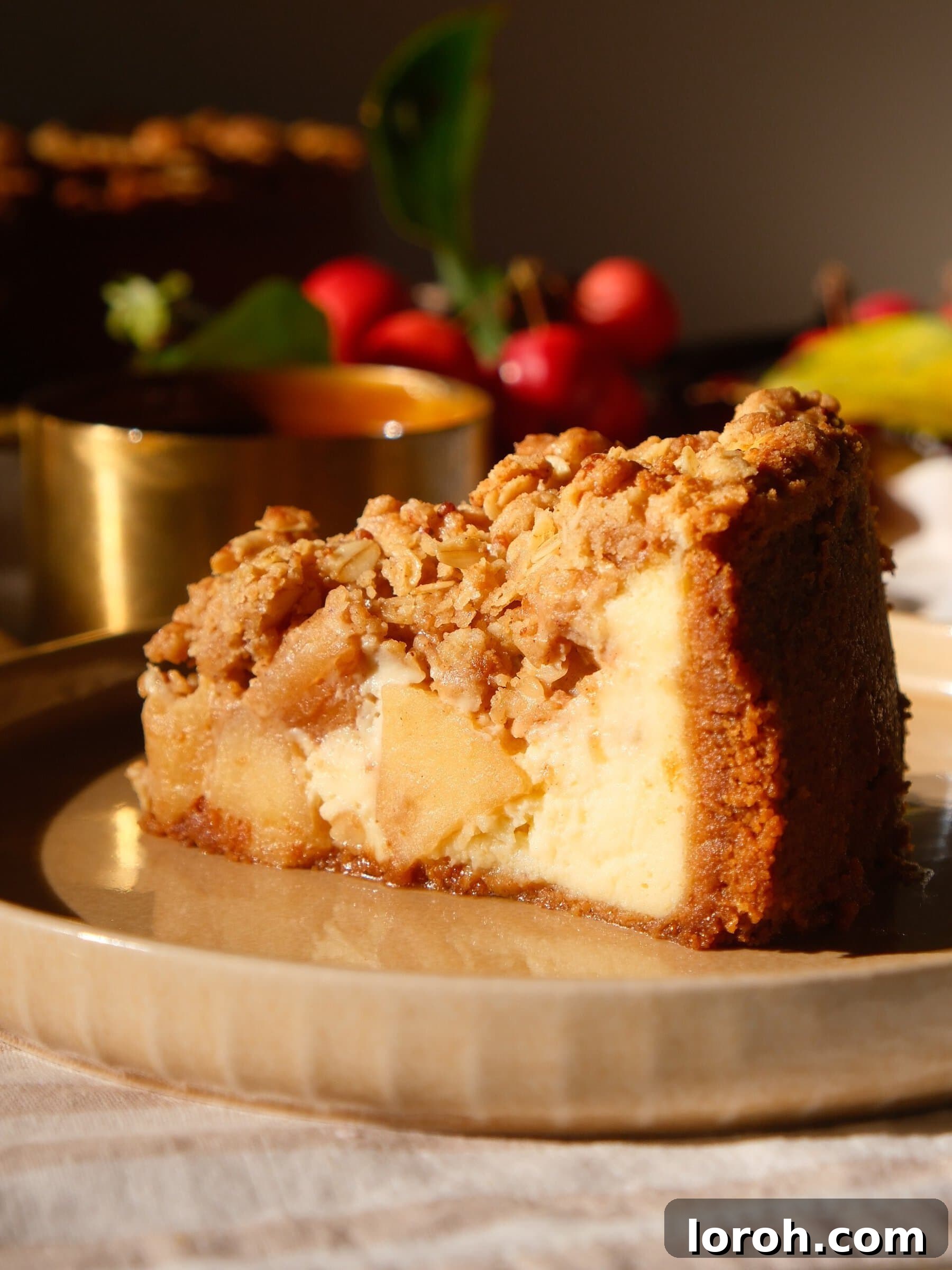 A beautifully presented slice of Apple Crumble Cheesecake, showing distinct layers of crust, cheesecake, apples, and crumble.