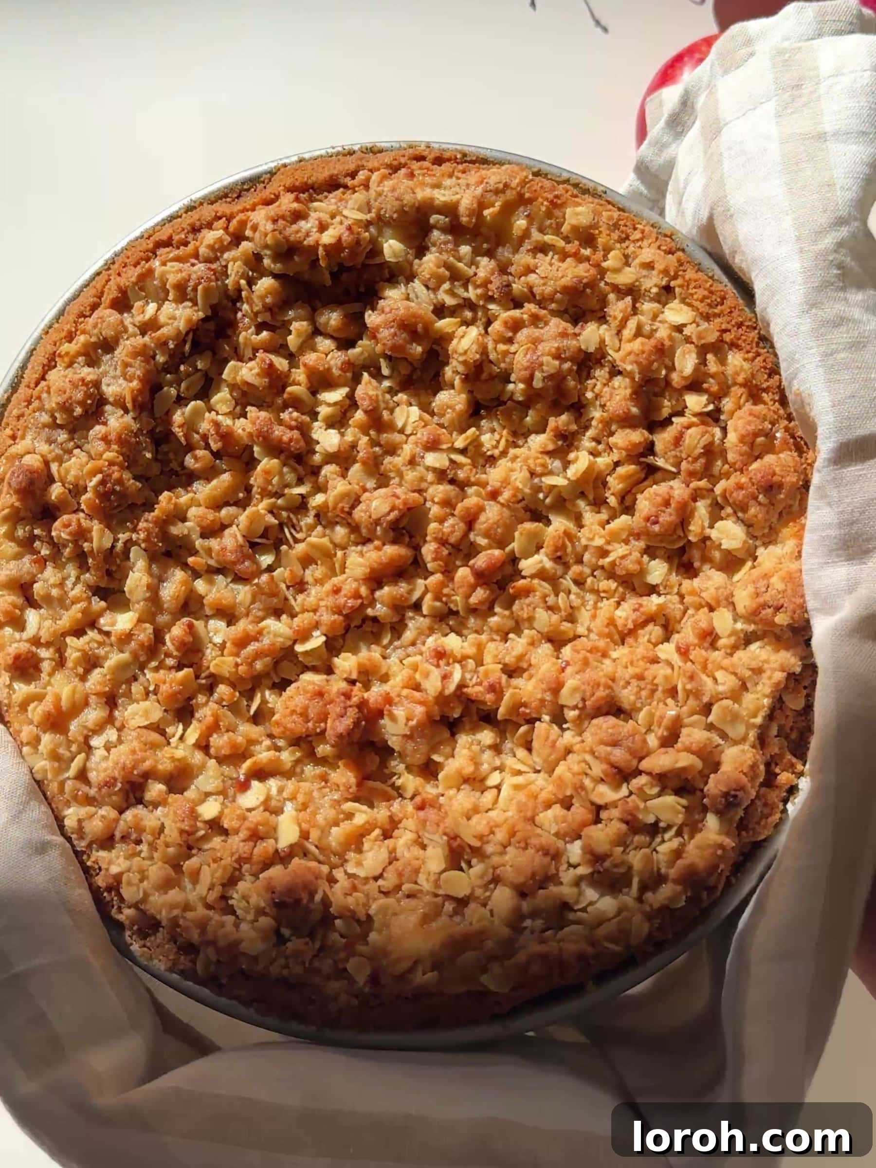 The Apple Crumble Cheesecake being carefully removed from the oven, showing its golden-brown crumble top.