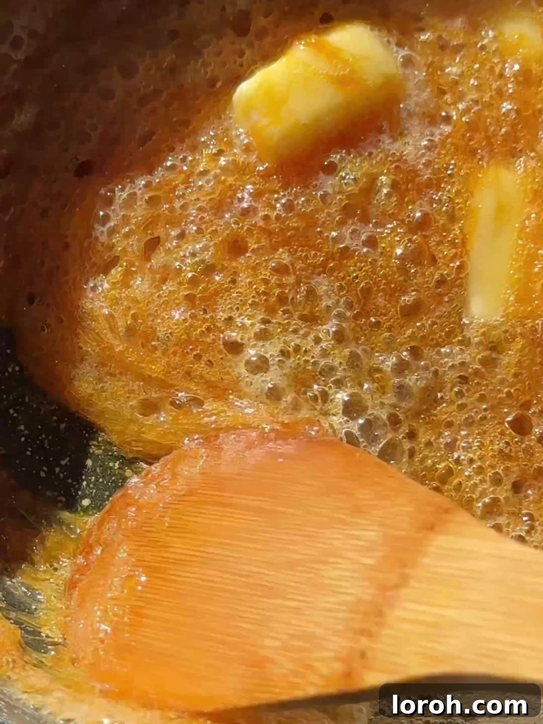 Diced unsalted butter being vigorously whisked into hot amber-colored caramel in a saucepan.