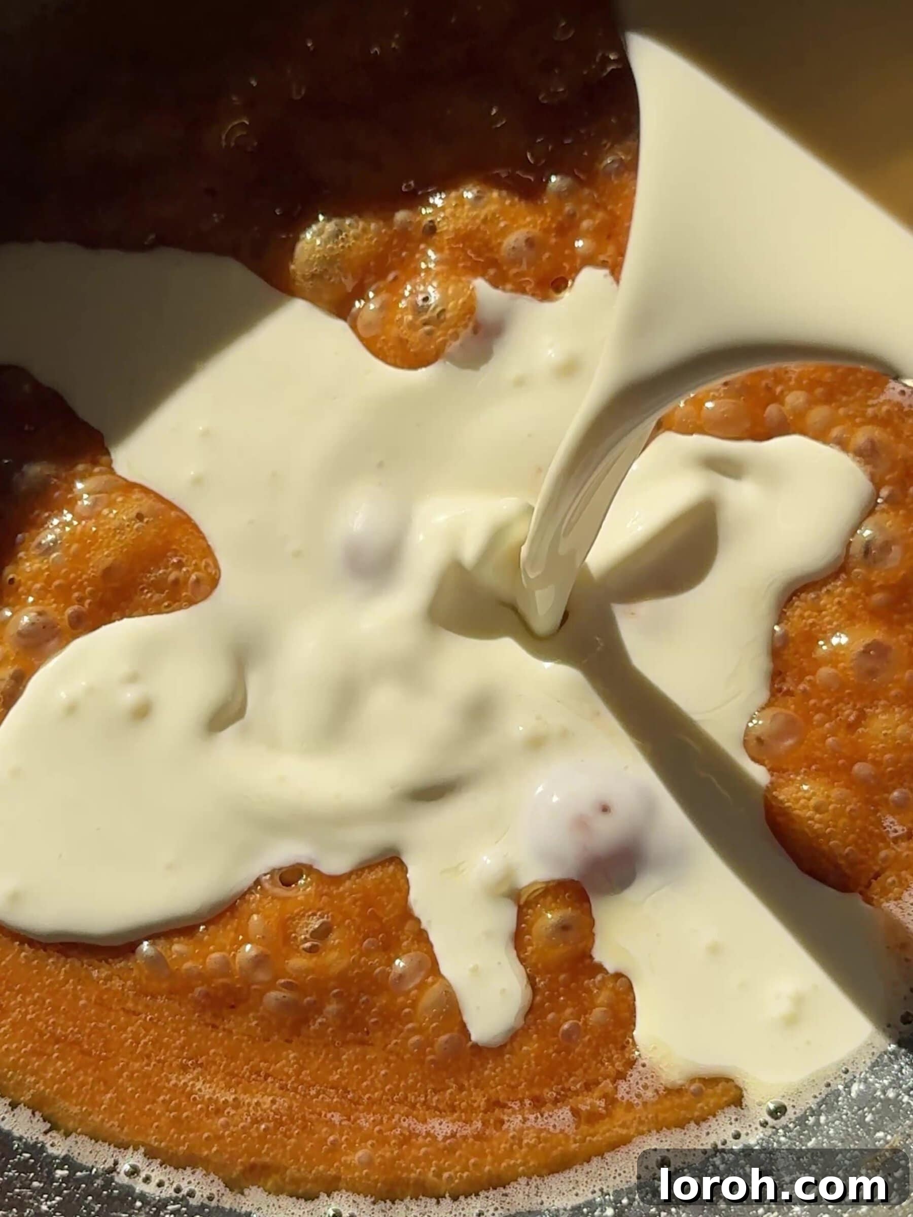 Double cream being slowly poured into the butter-caramel mixture while whisking, to create a smooth, glossy sauce.