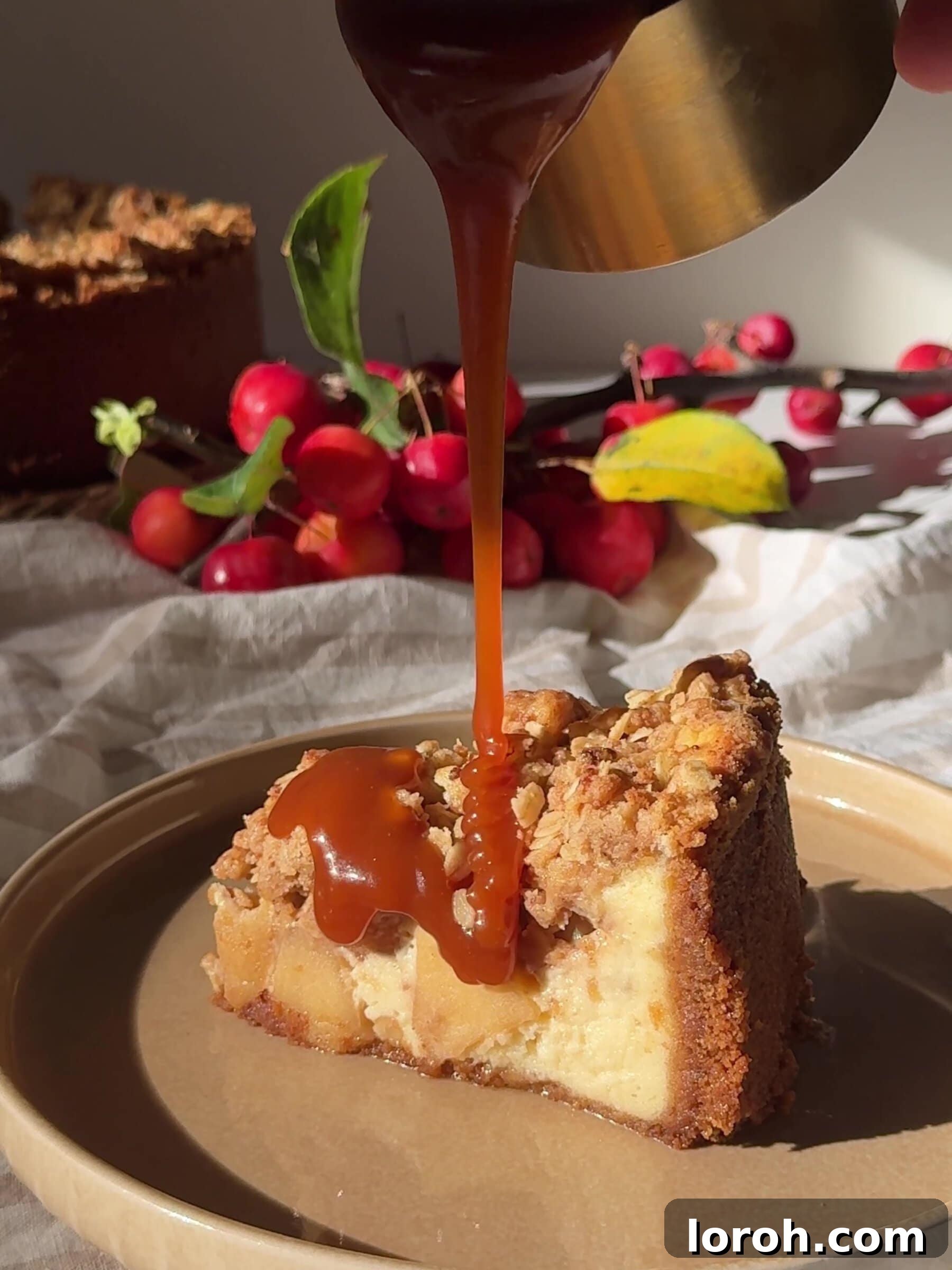 A slice of Apple Crumble Cheesecake being drizzled with warm, glistening salted caramel sauce.
