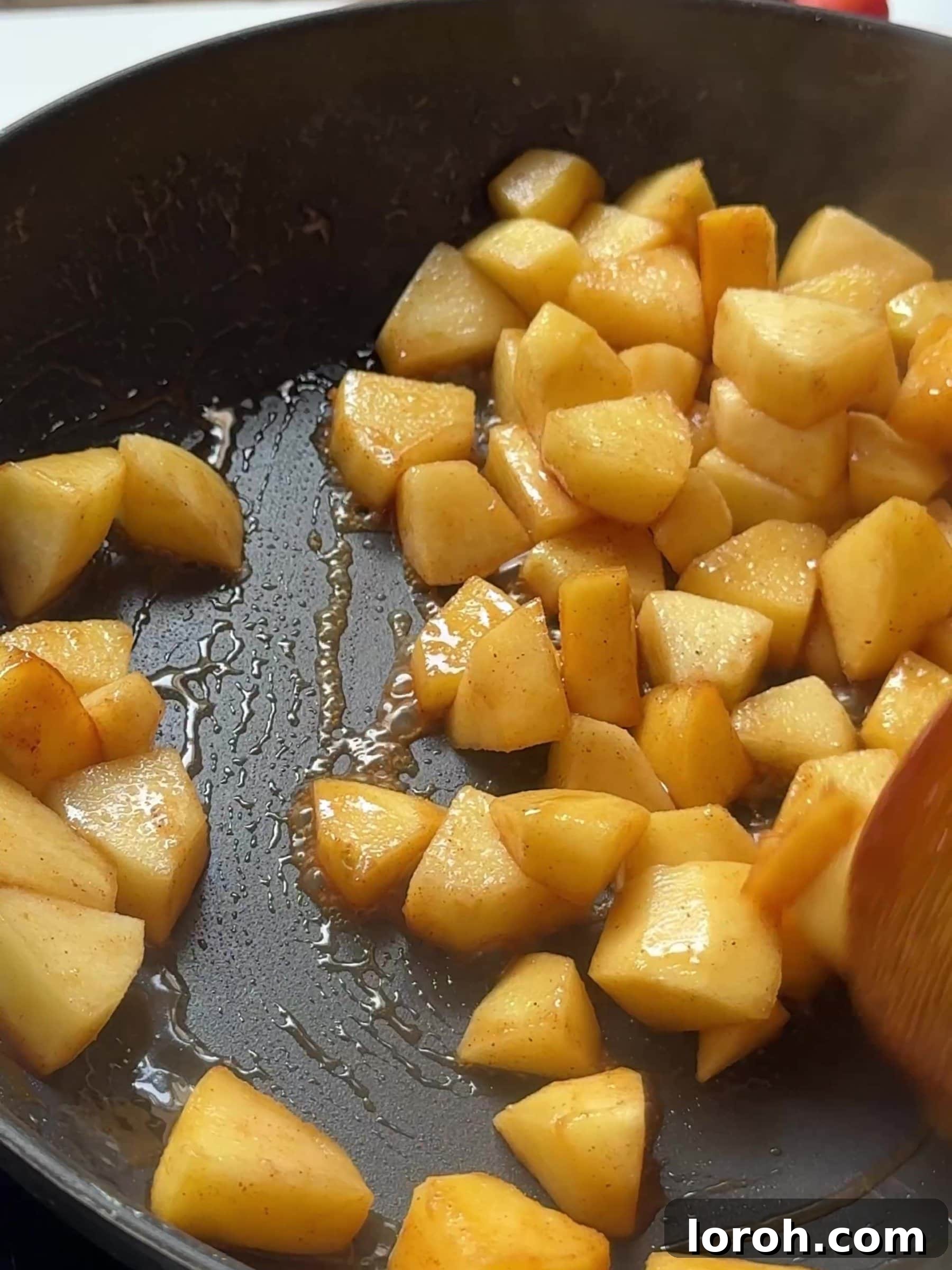 Diced apples cooking gently in a frying pan with butter, sugar, and cinnamon, creating a spiced apple filling.
