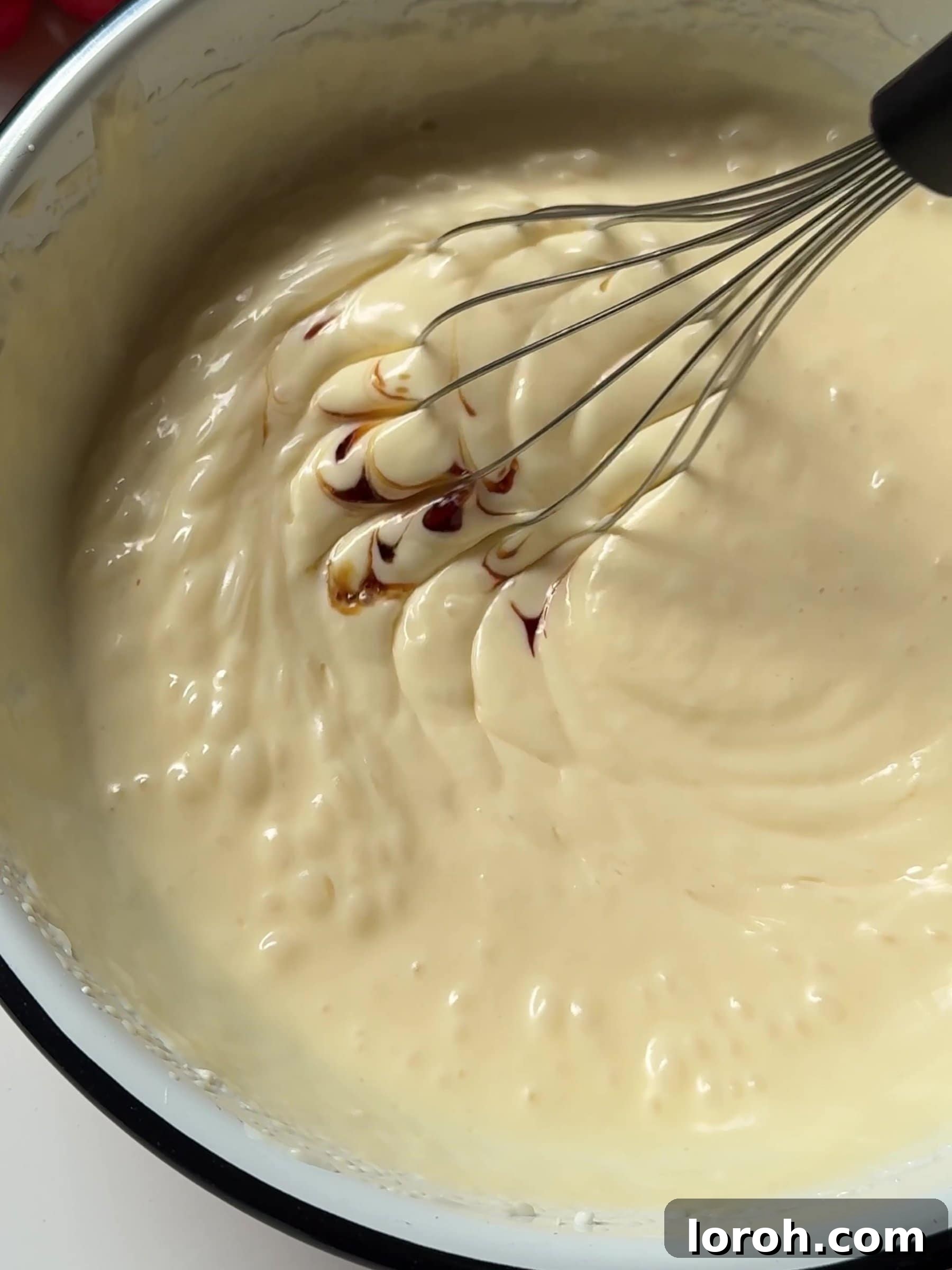 Cream cheese being beaten in a mixing bowl, then vanilla extract is added, creating a smooth cheesecake batter.