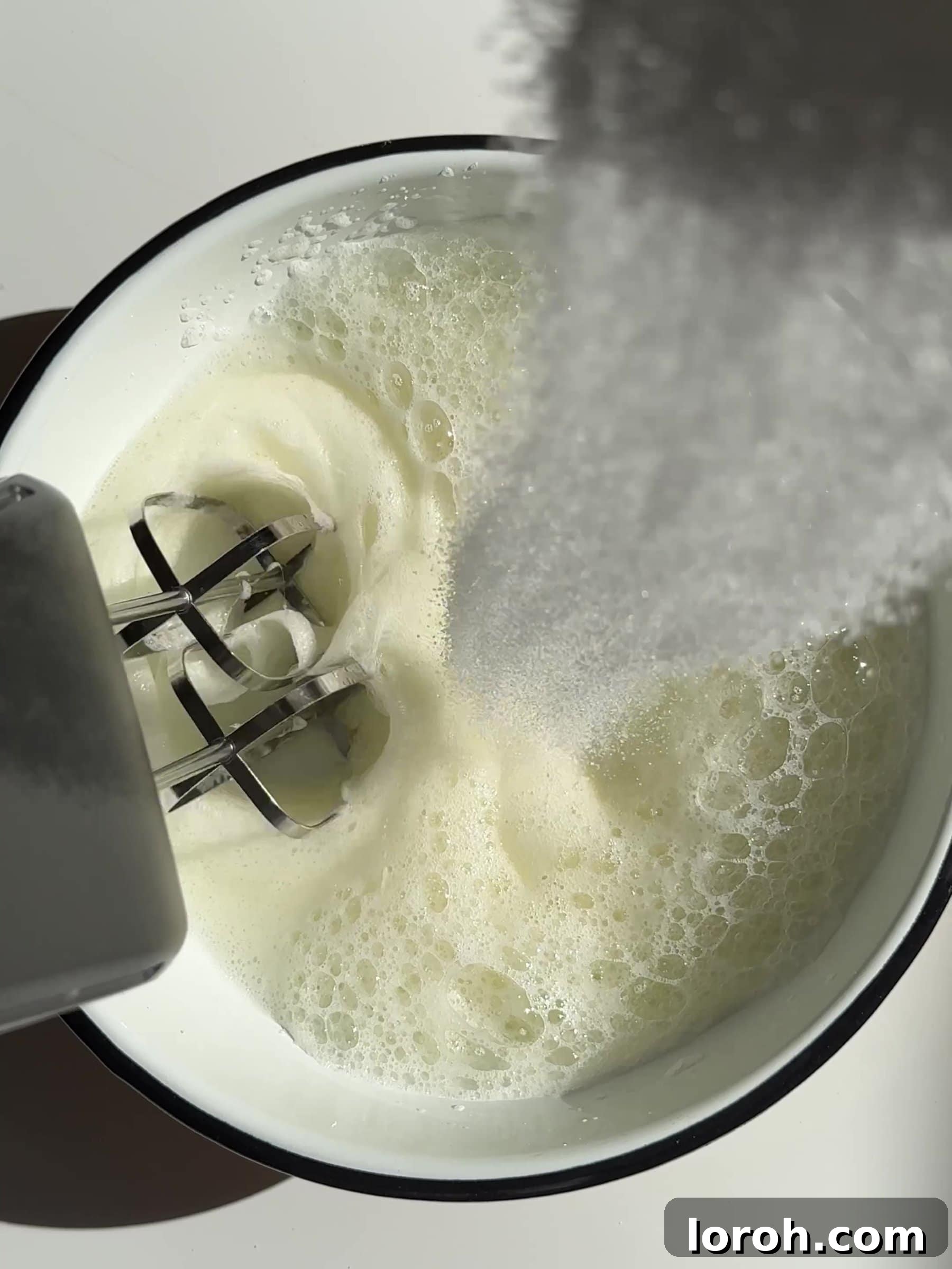 Whisking caster sugar into egg whites to create stiff peaks for Moelleux au Chocolat.
