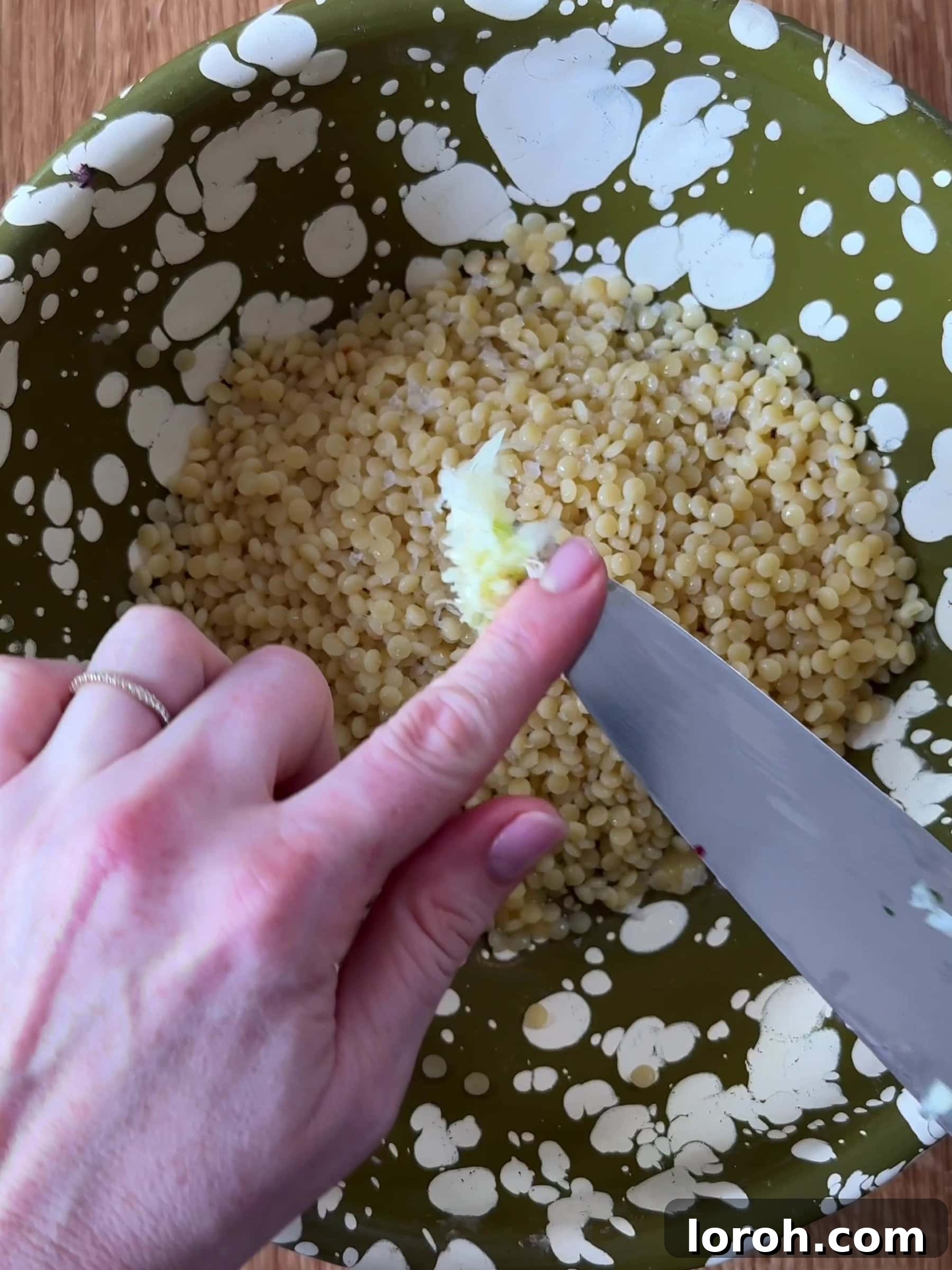 Golden Lamb & Couscous with Bright Herb Salad 7 Crushed garlic and olive oil being added to cooked giant couscous in a bowl.