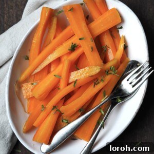White serving dish of glazed carrots with fresh thyme sprinkled over the top.