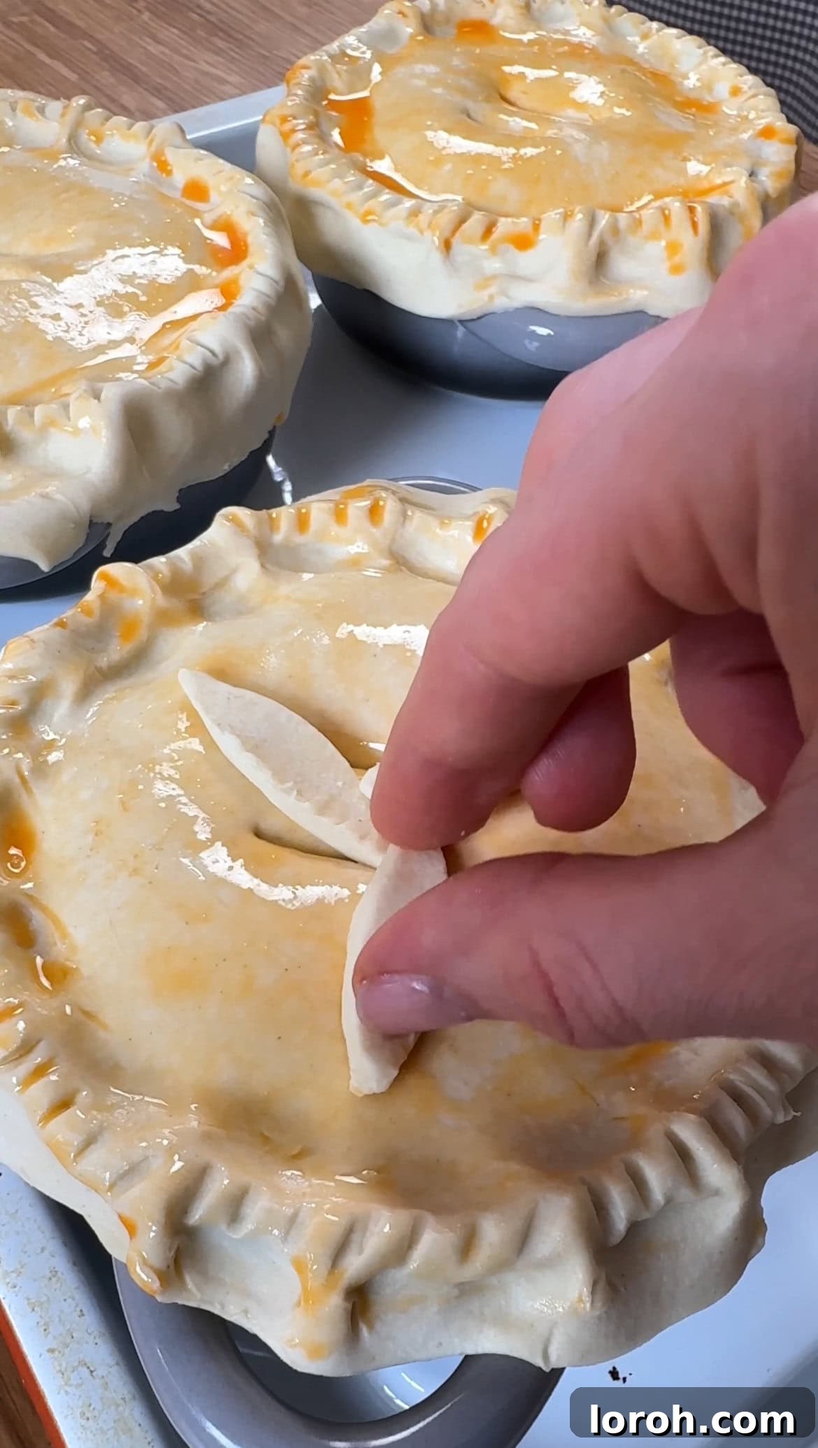 A puff pastry lid laid over a ramekin, crimped with a fork, and decorated with a small leaf-shaped pastry cut-out before baking.
