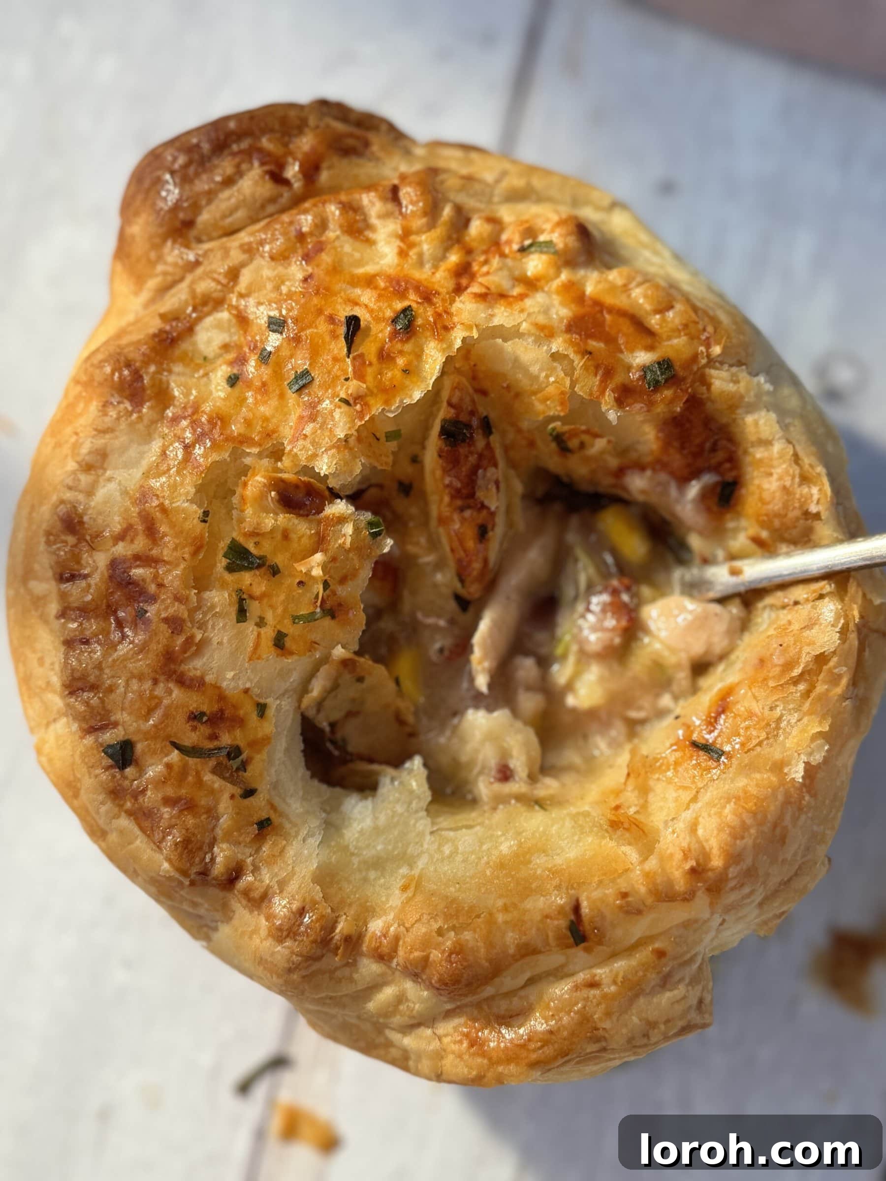 A chicken mini pot pie with a spoon scooping out a portion, highlighting the creamy filling and flaky crust.