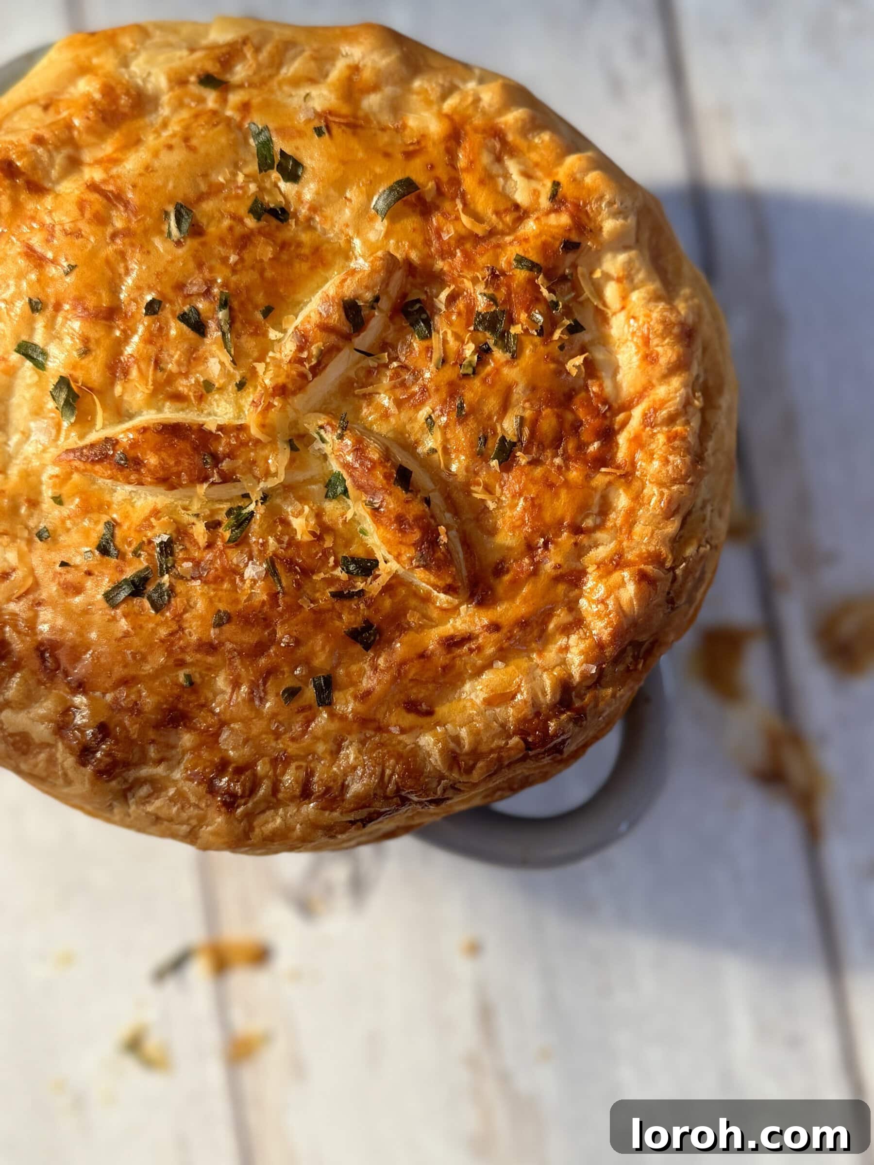 A close-up of a chicken mini pot pie, showing the golden, crimped puff pastry crust and the creamy filling peeking through the steam vents.