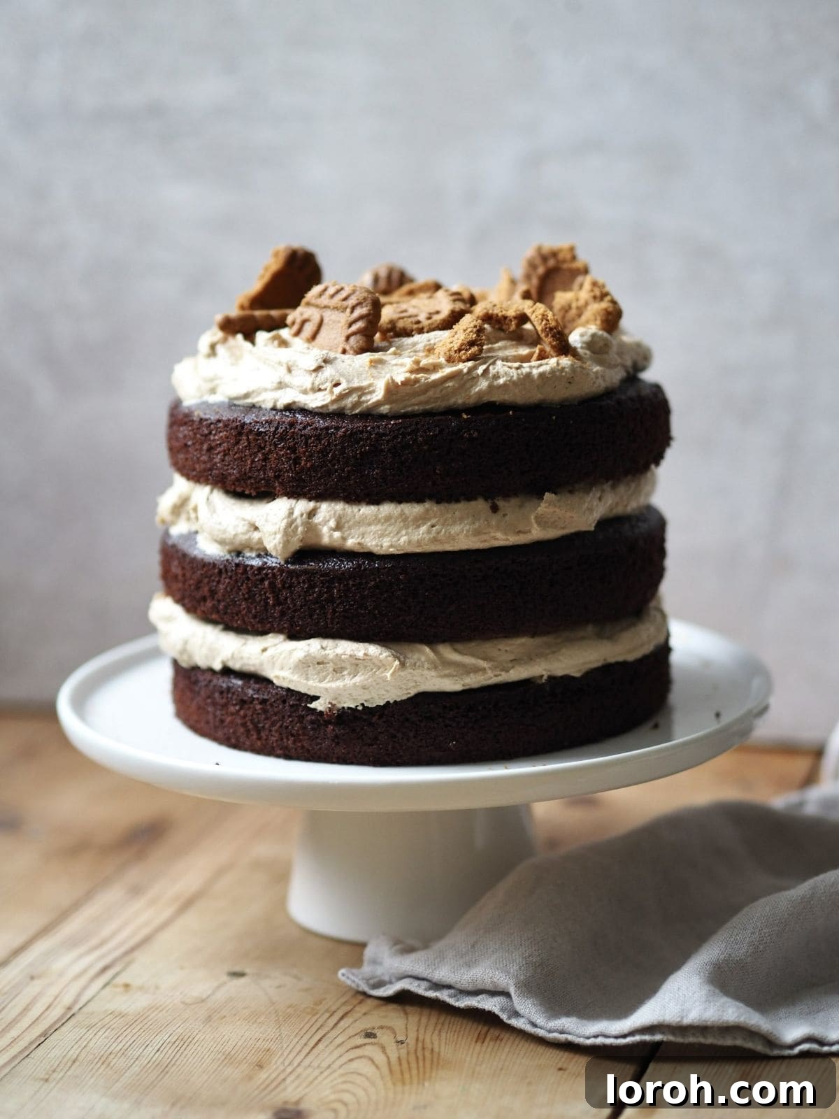 A whole Easy Biscoff Cake sitting elegantly on a pristine white cake stand, ready to be sliced and enjoyed.